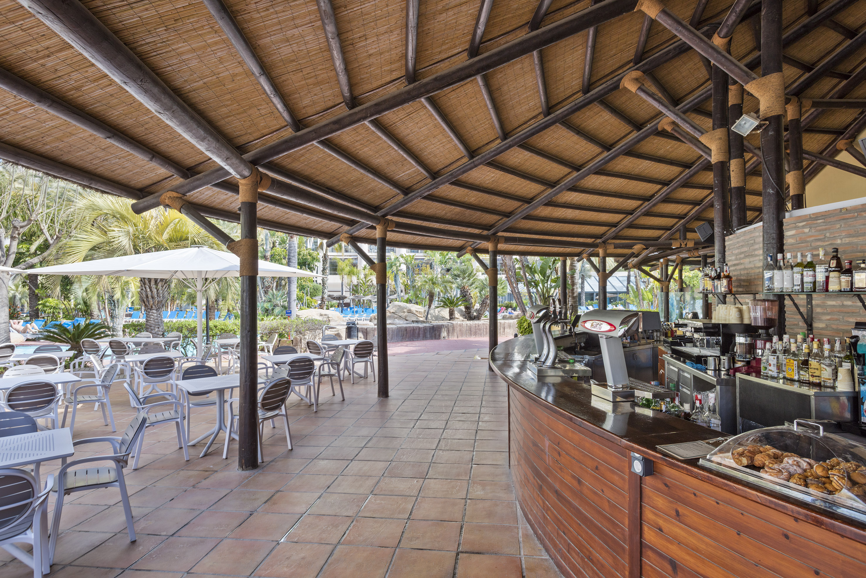 Resort outdoor bar with thatched roof, wooden counter, and poolside seating.
