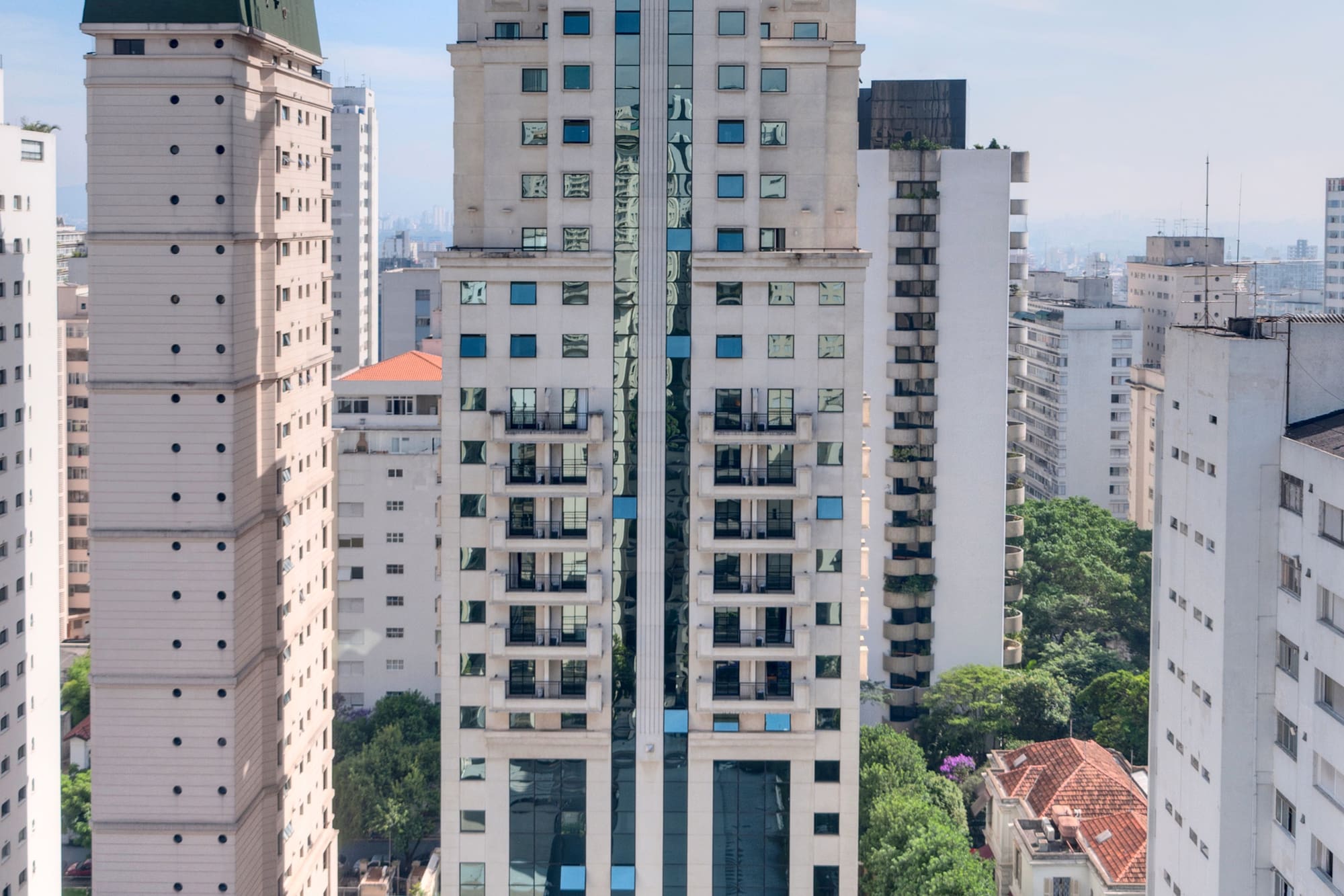White skyscraper with green roof, reflective windows, and swimming pool.