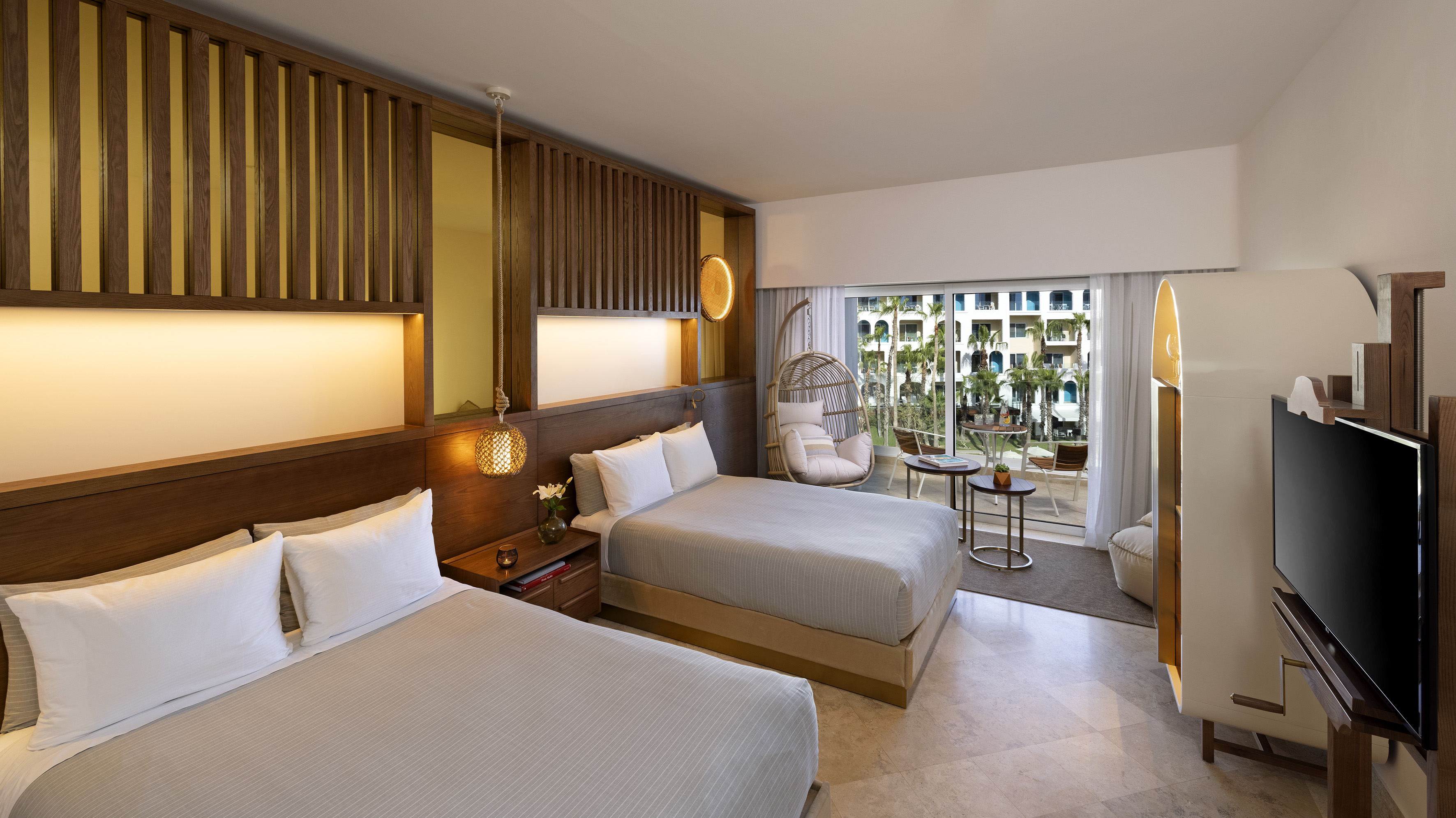 Hotel room with two beds, modern wood decor, balcony, and tropical view.