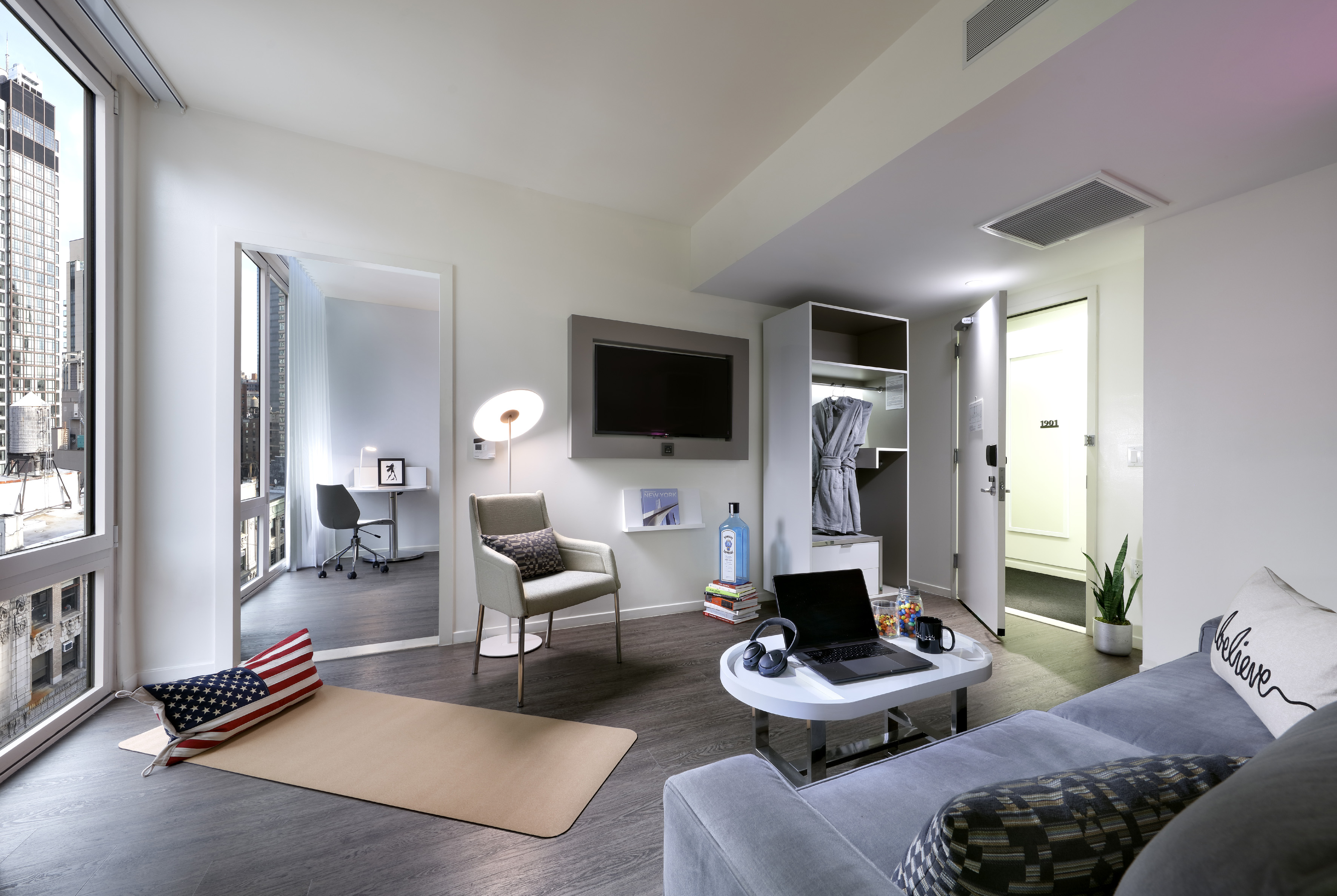 Modern urban apartment living area with city view, sofa, TV, and desk.