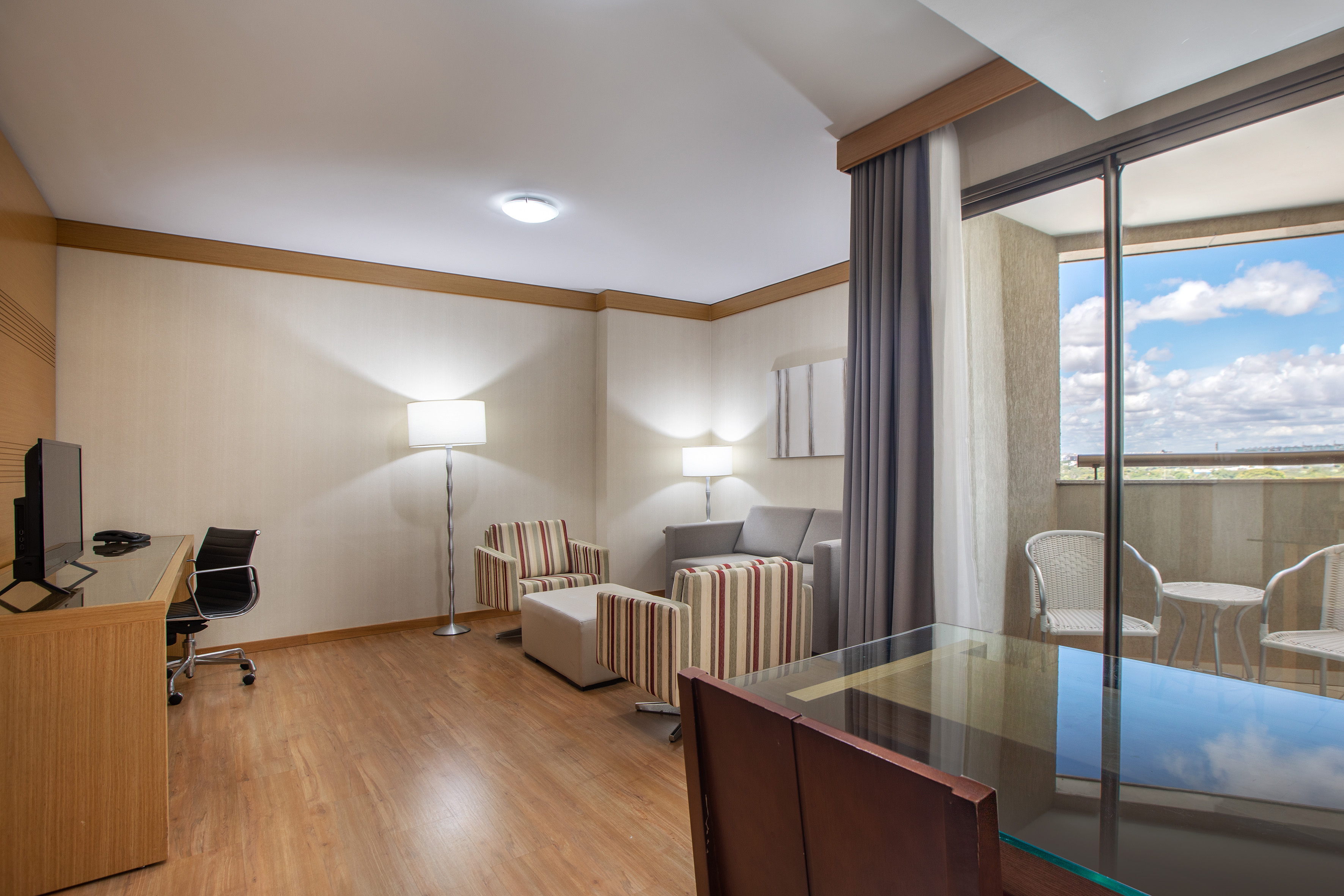 Hotel suite living room with desk, sofa, armchairs, and balcony.