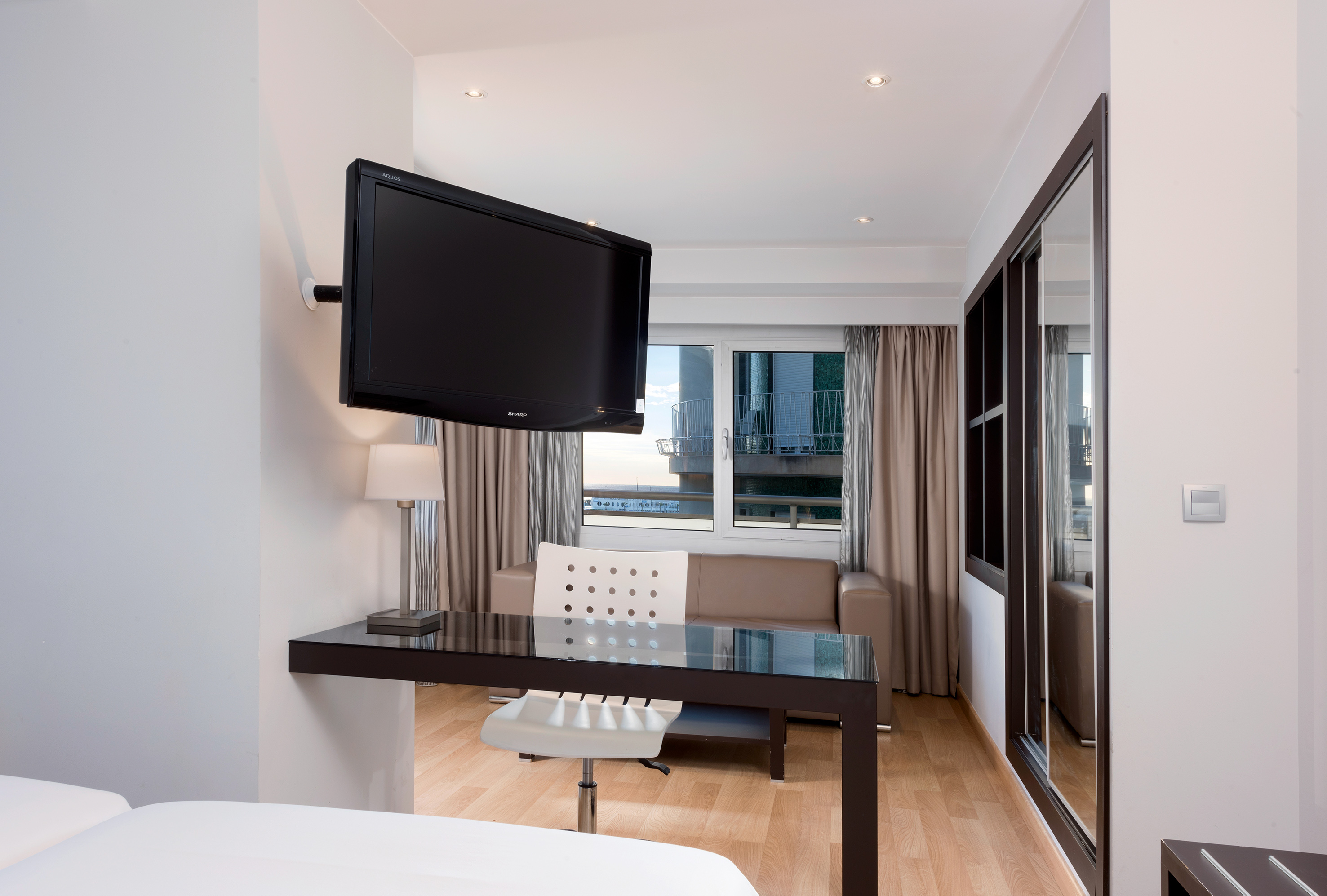 Modern hotel room with wall-mounted TV, work desk, and sofa by window.