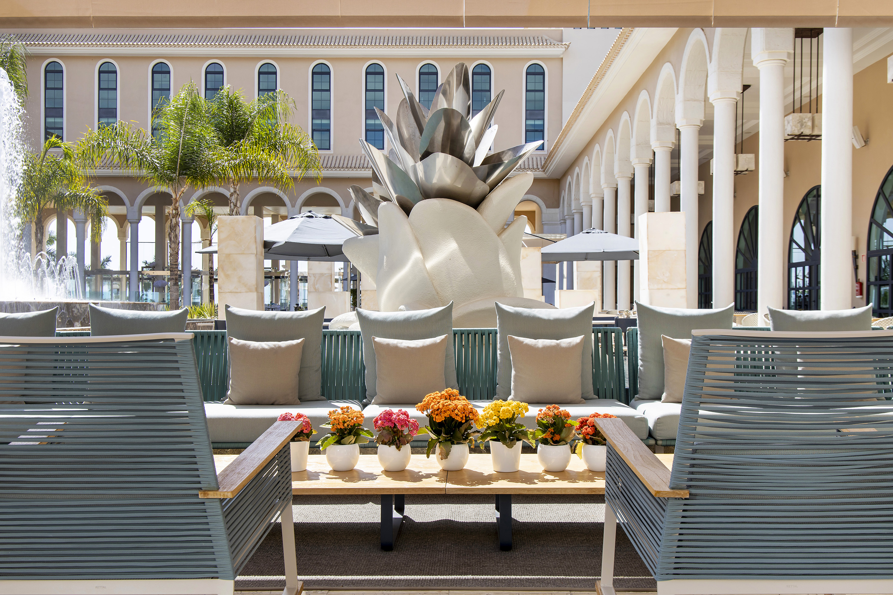 Luxury patio with modern seating, colorful flowers, and large agave sculpture.