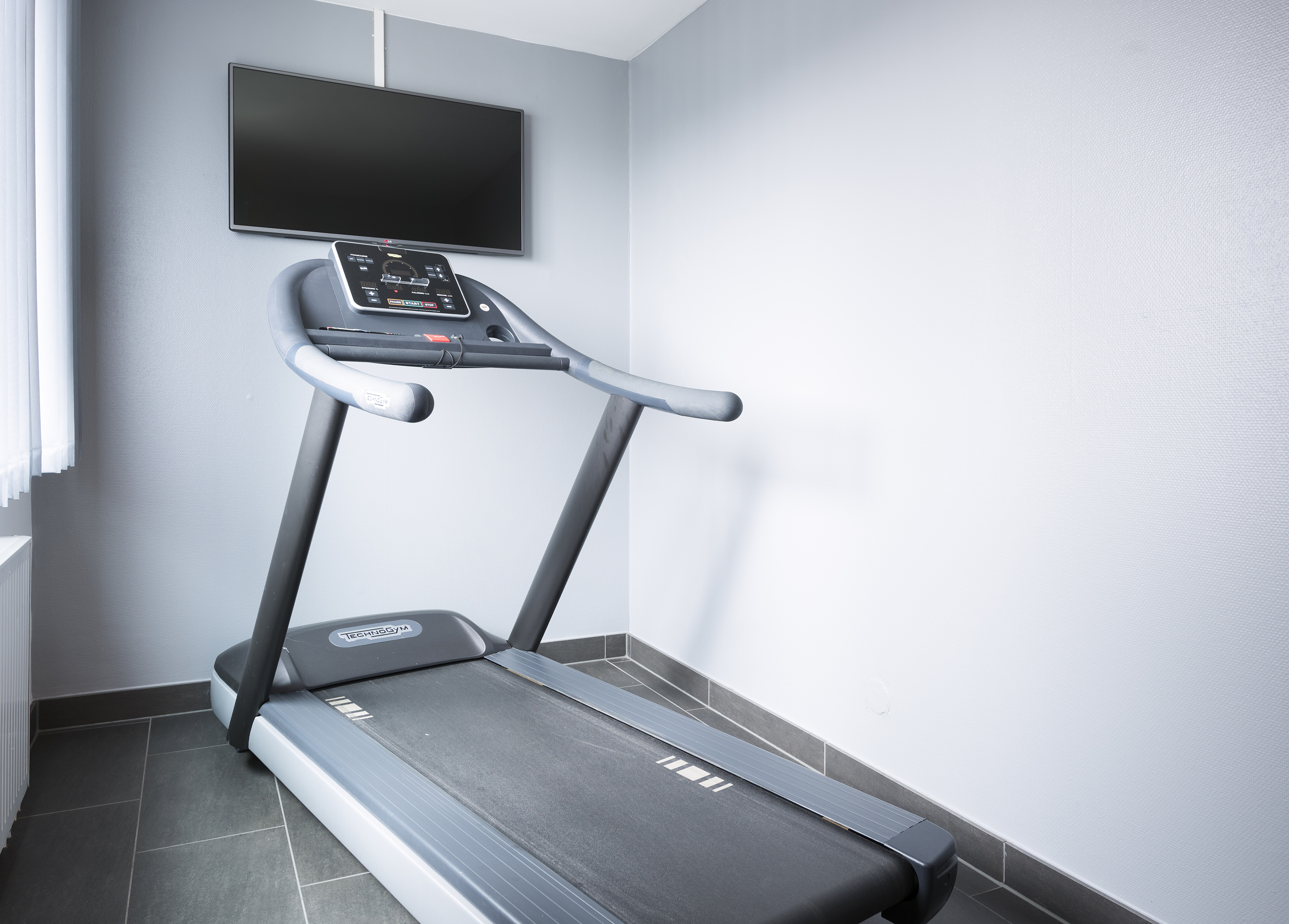 Technogym treadmill with wall-mounted TV in a modern fitness room.