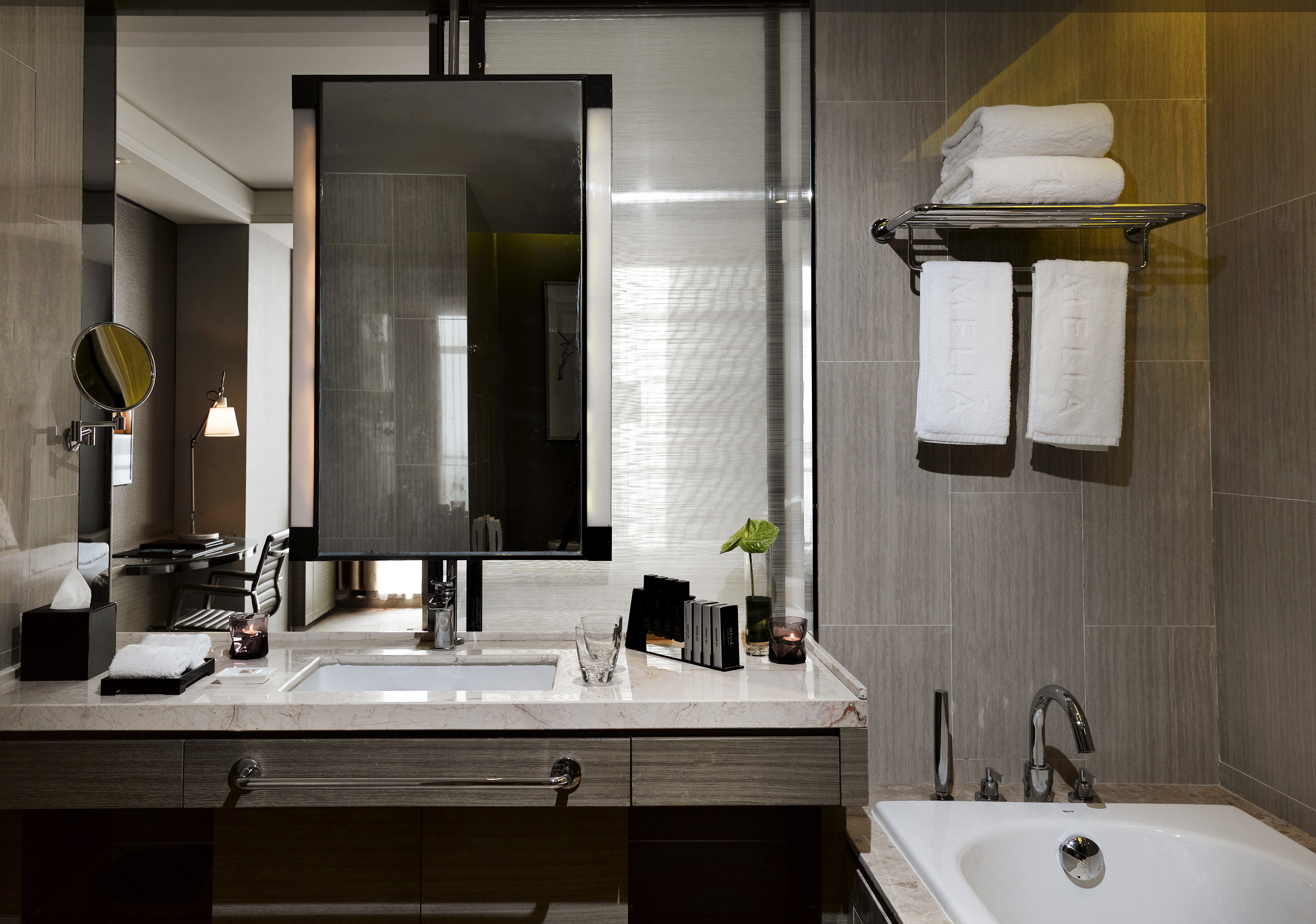 Modern hotel bathroom with marble vanity, mirror, sink, bathtub, and white towels.