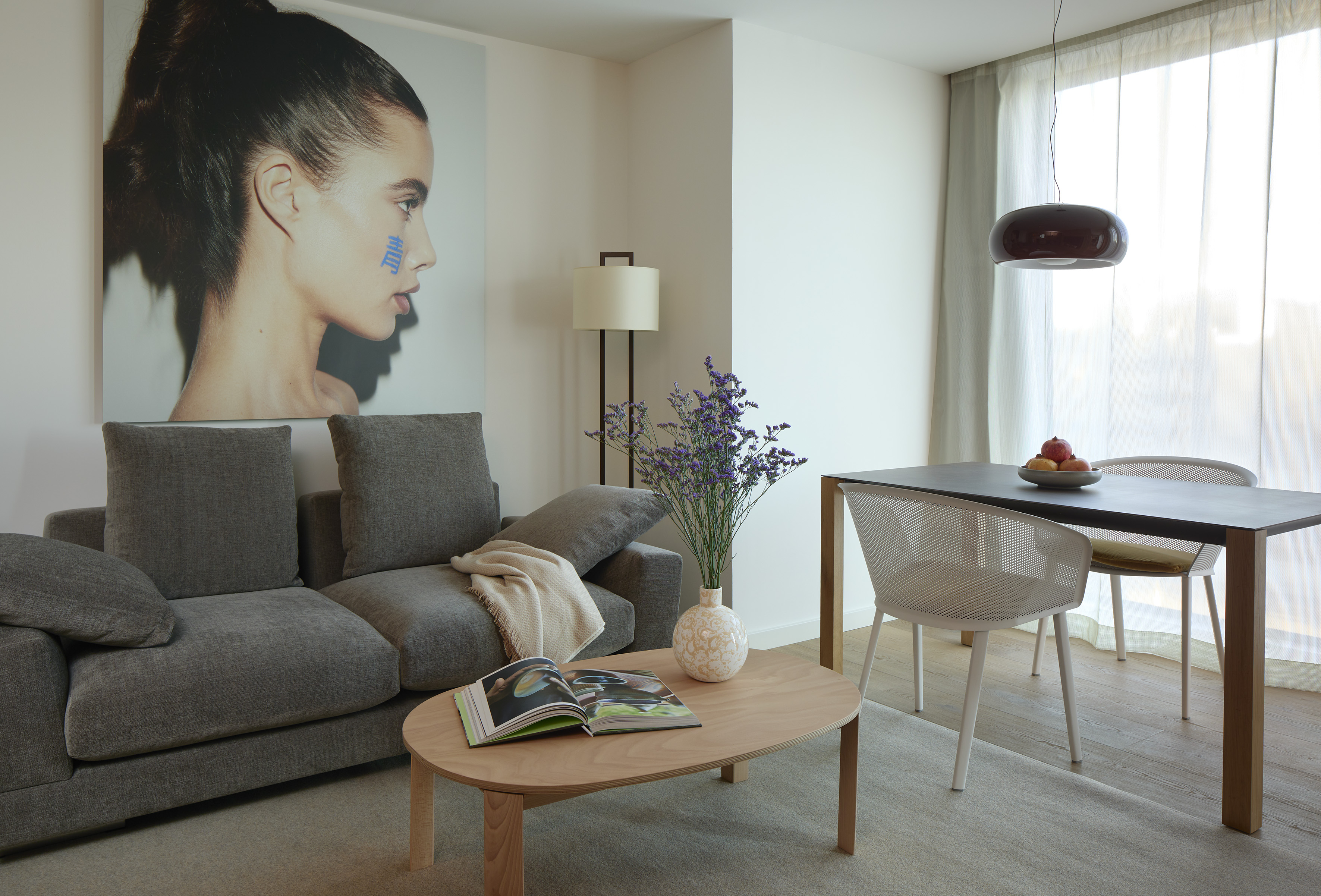 Modern living & dining room with gray sofa, wooden tables, and portrait art.