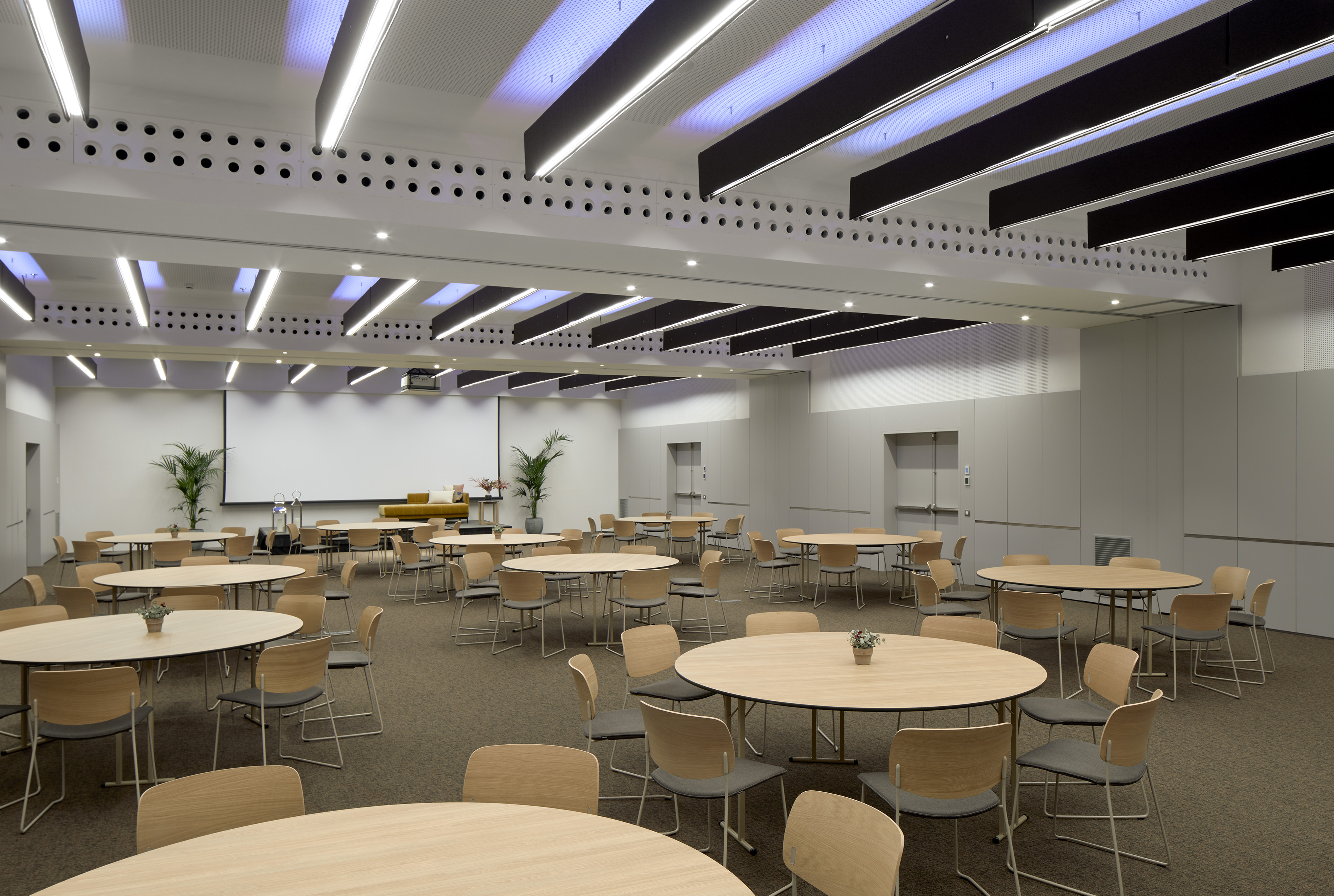 Modern conference event room with round tables, chairs, and projector screen.
