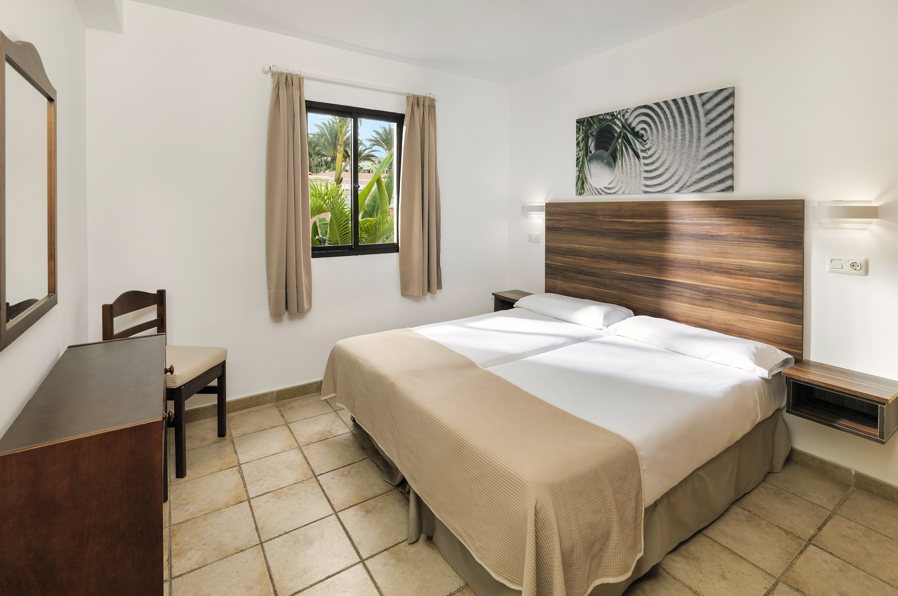 Resort bedroom with two beds, wooden headboard, window, tropical palm view.