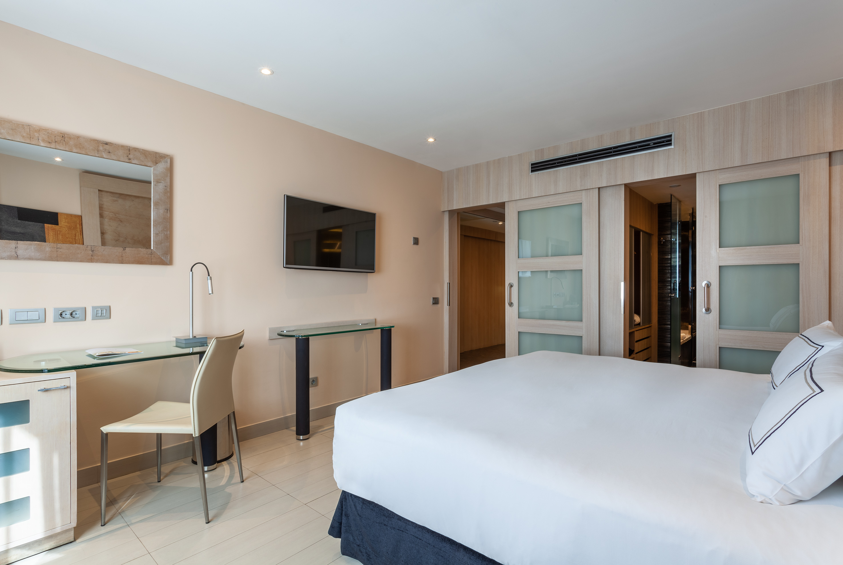 Modern hotel room with bed, desk, wall-mounted TV, and sliding closet doors.