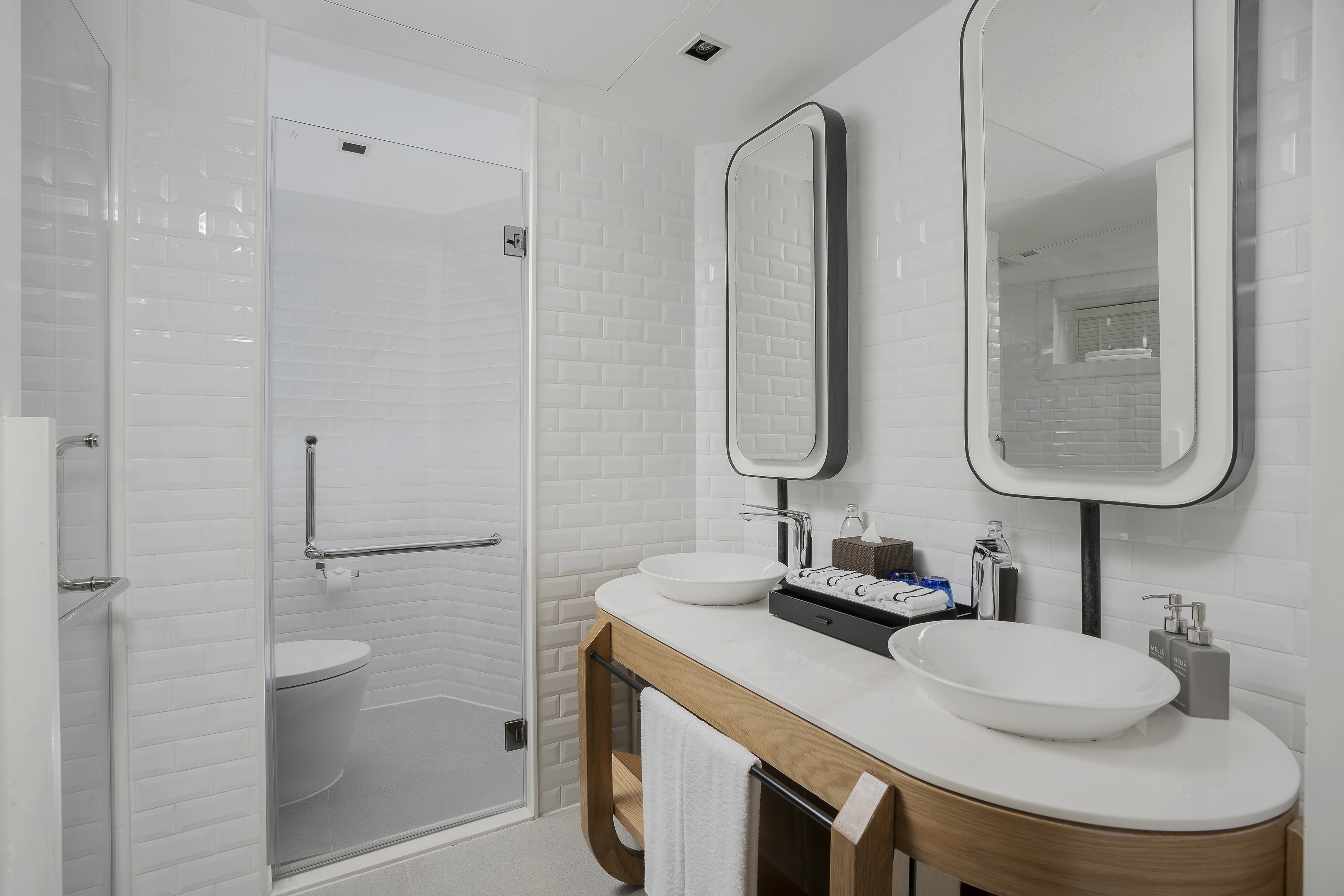 Modern hotel bathroom, double vanity, vessel sinks, white tiles, glass shower.