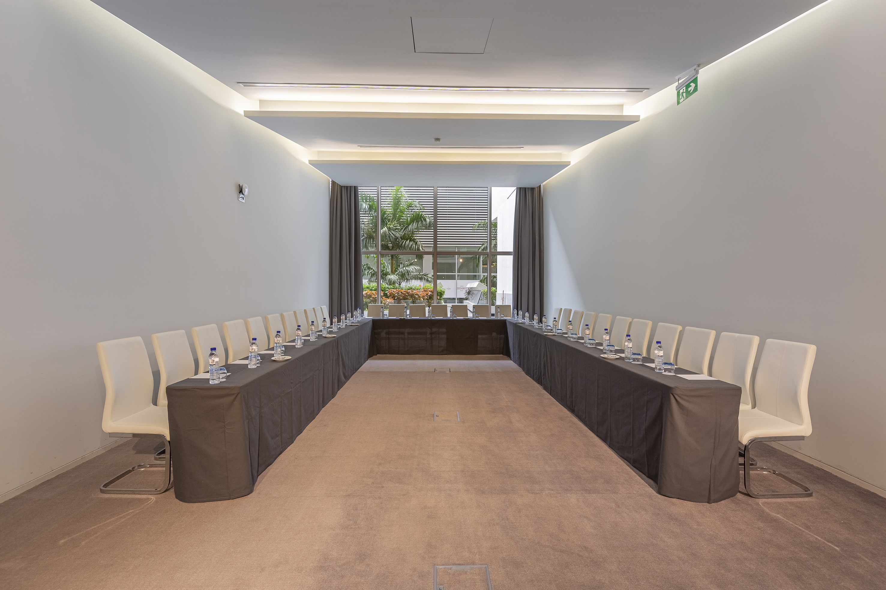 Modern U-shaped conference room with white chairs, large window, and palm trees. - Sala Sommerschield - Meliá Maputo Sky, Maputo