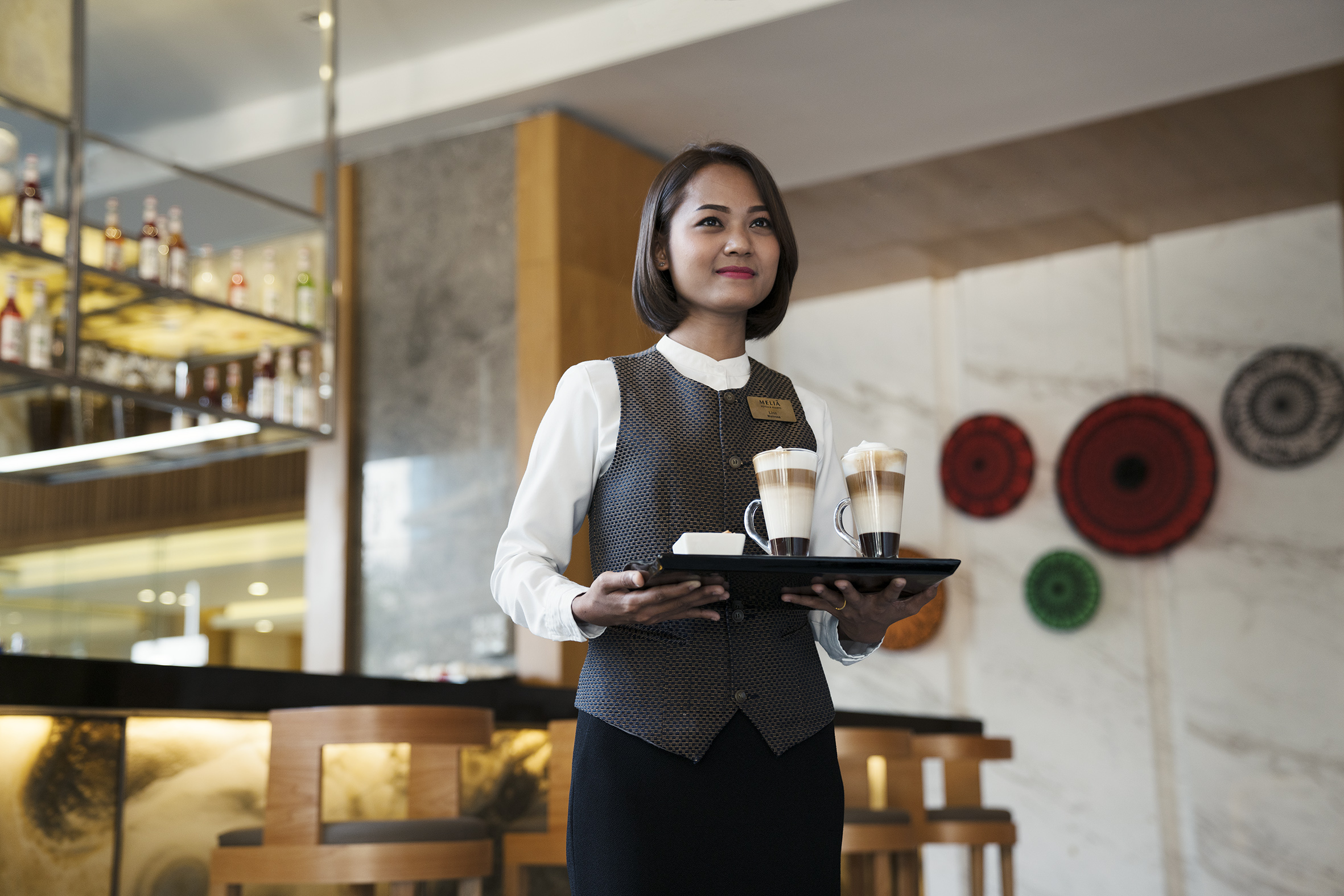 Melia server carrying lattes on a tray in a modern hotel bar.