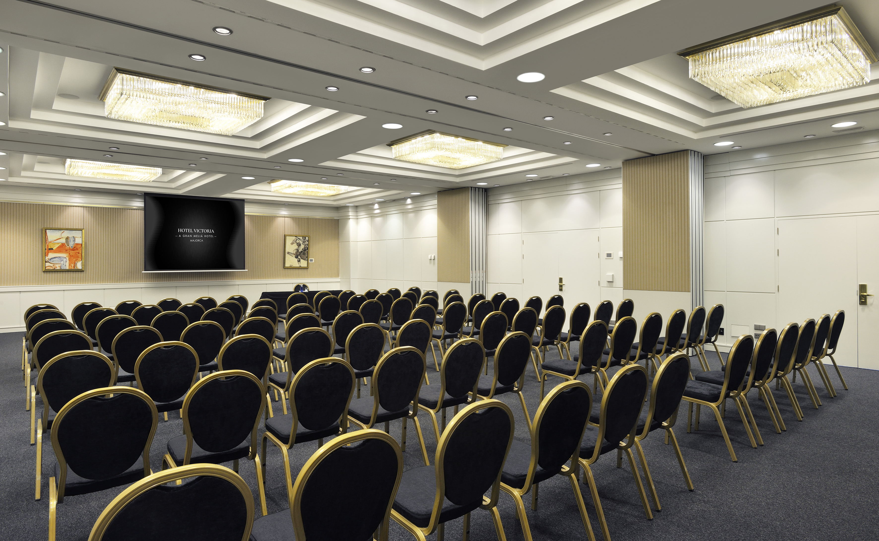 Hotel Victoria meeting room with screen, rows of chairs, and chandeliers.