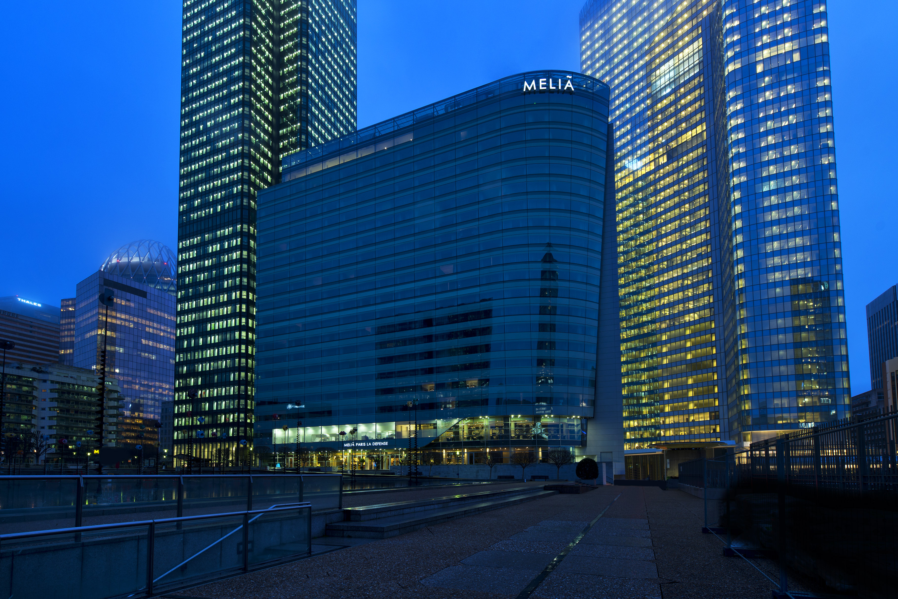 Illuminated Meliã Paris La Defense hotel and modern skyscrapers at blue hour.