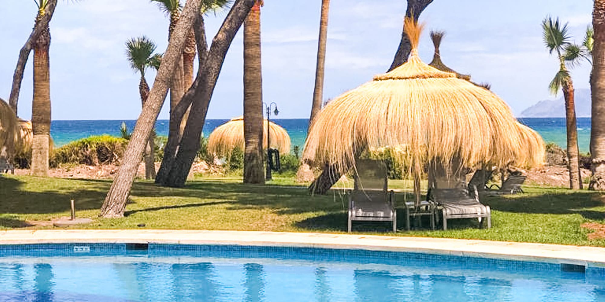 a pool with grass huts and trees