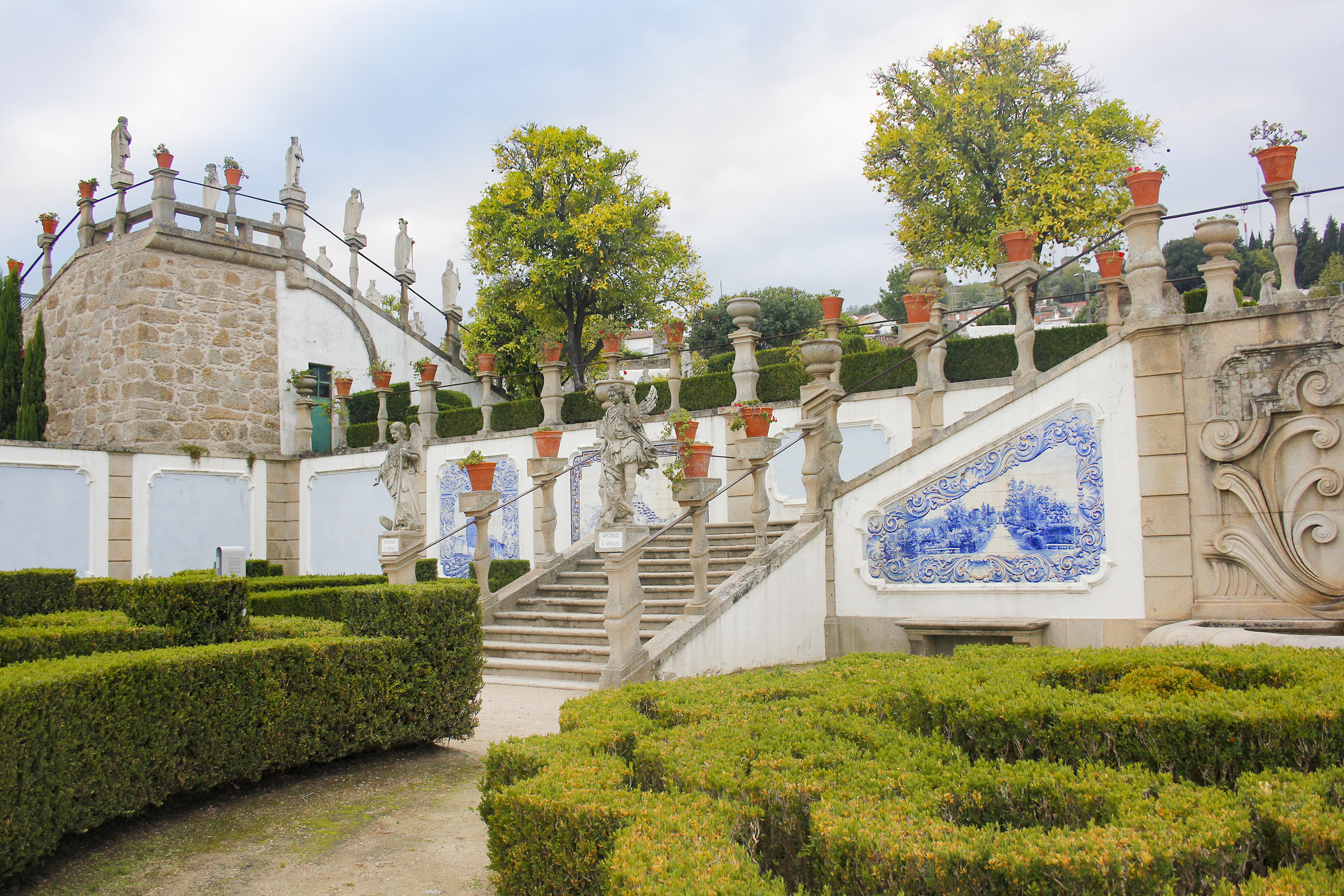 Baroque garden with stone staircase, azulejo tiles, statues, and sculpted hedges.