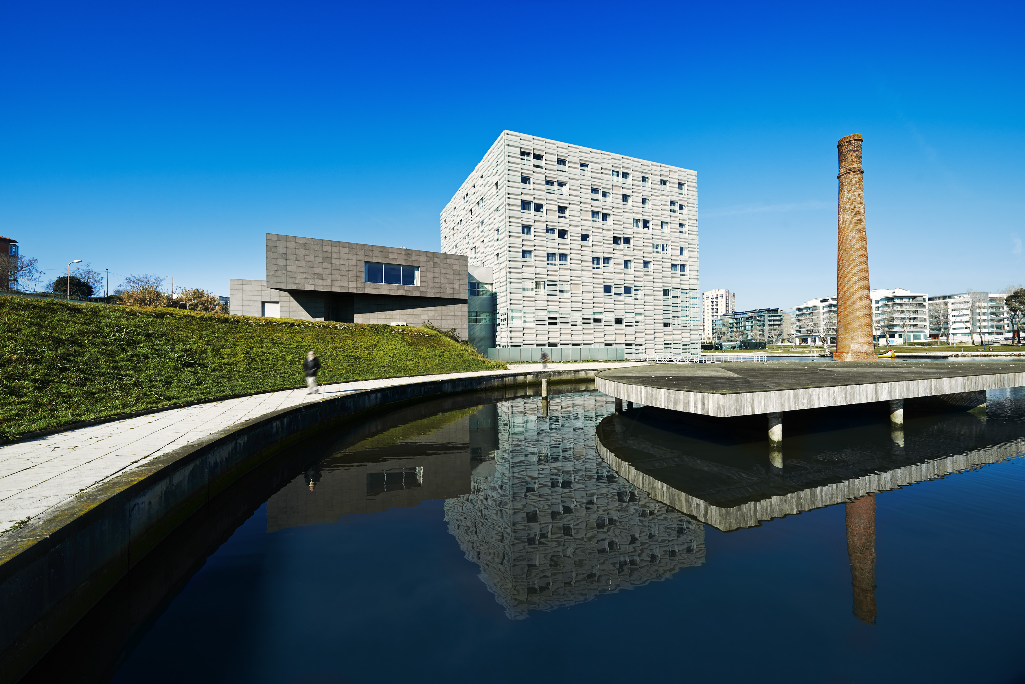 Modern architecture, industrial chimney, and reflections in urban waterfront.