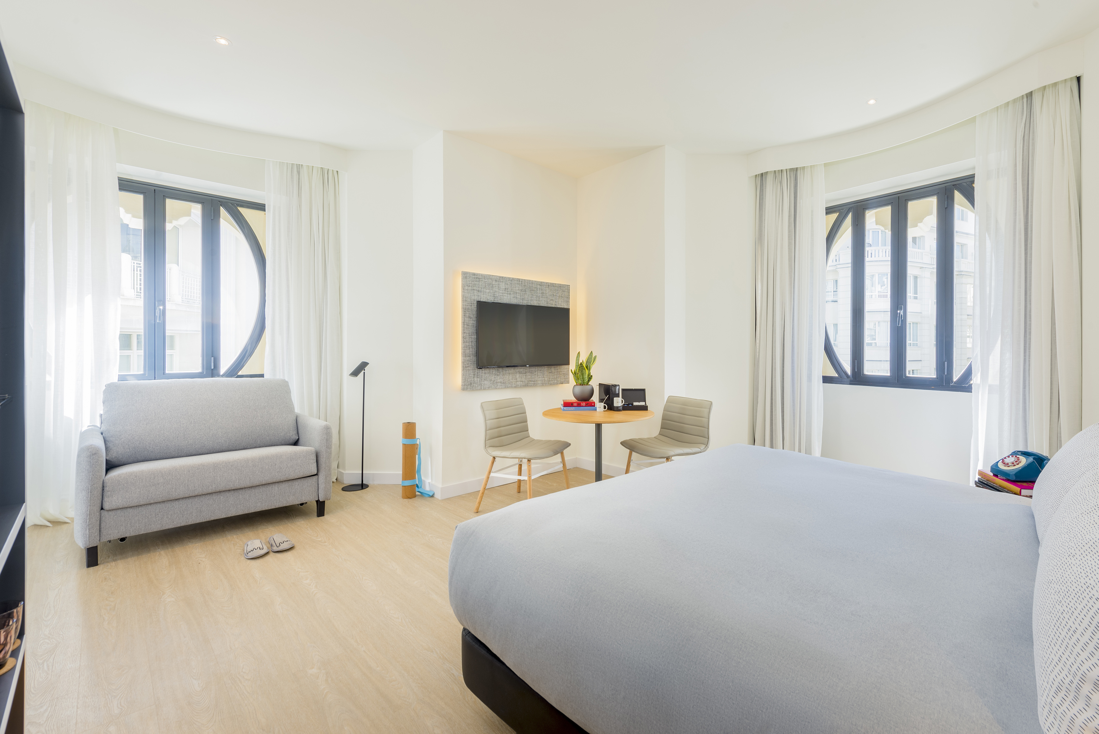 Modern hotel room with large bed, sofa, TV, and distinctive curved windows.