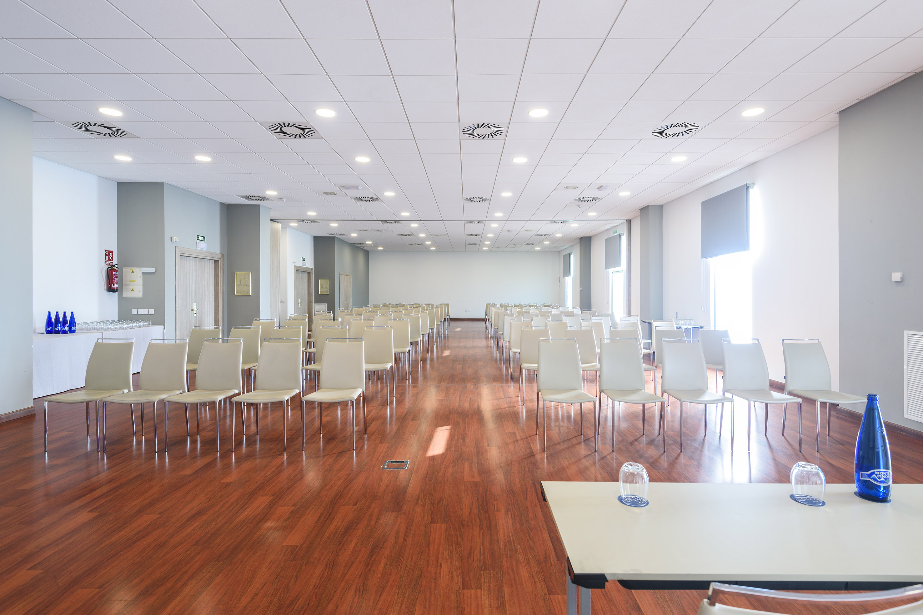 Modern empty conference room with rows of chairs, wooden floor, and refreshments.