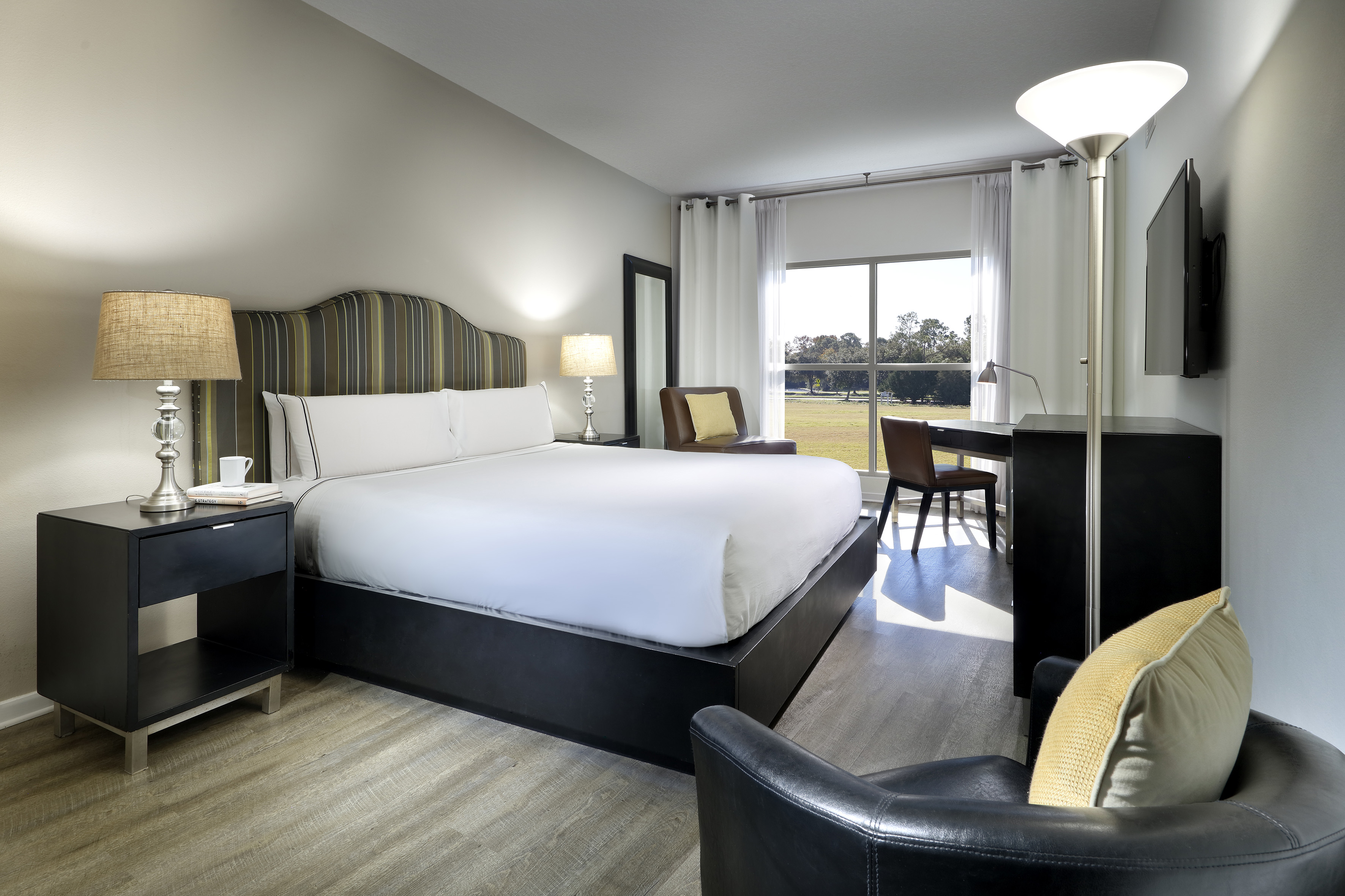 Modern hotel room with king bed, work desk, and scenic window view of green landscape.