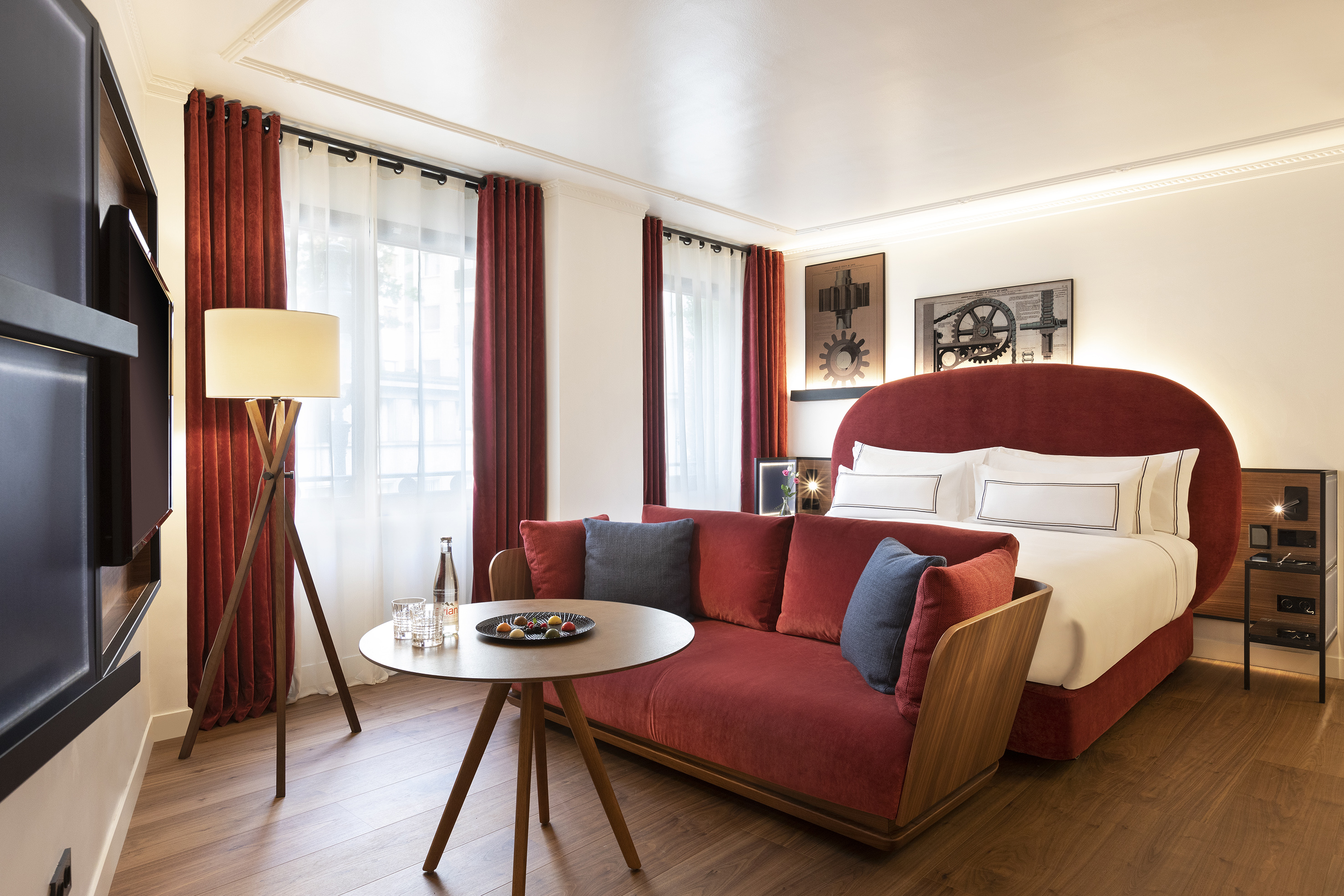 Hotel suite with red velvet bed, sofa, wood floor, and industrial gear art.