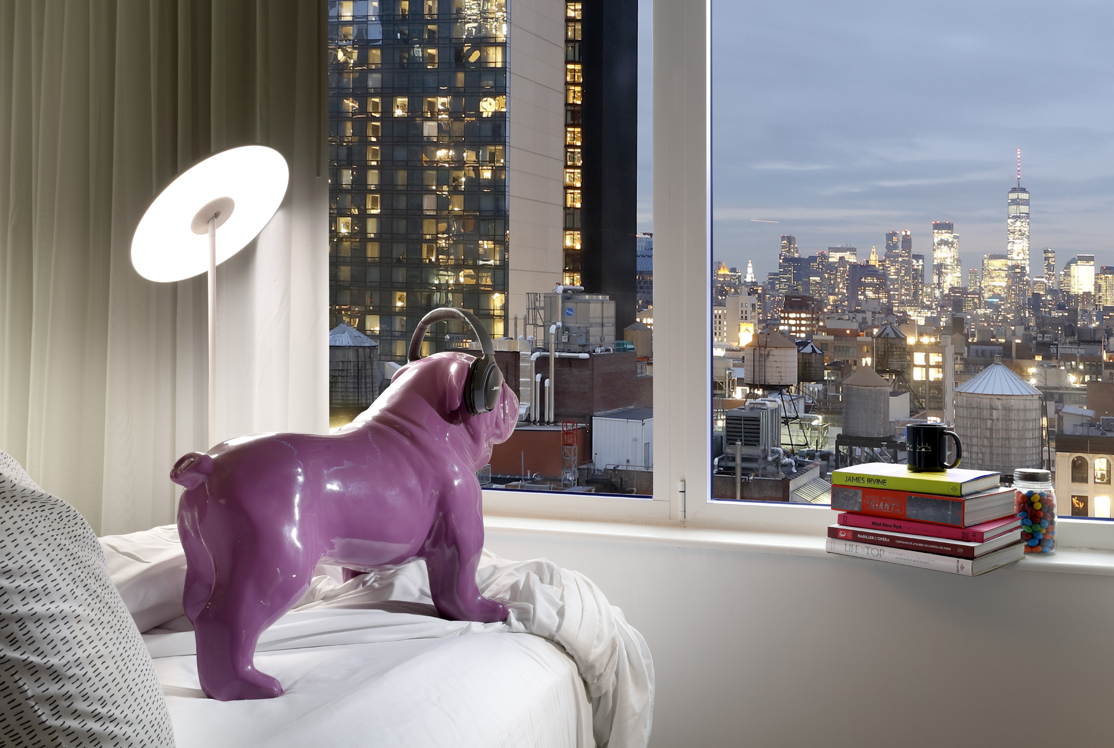 Purple bulldog with headphones watches illuminated NYC skyline from hotel room.