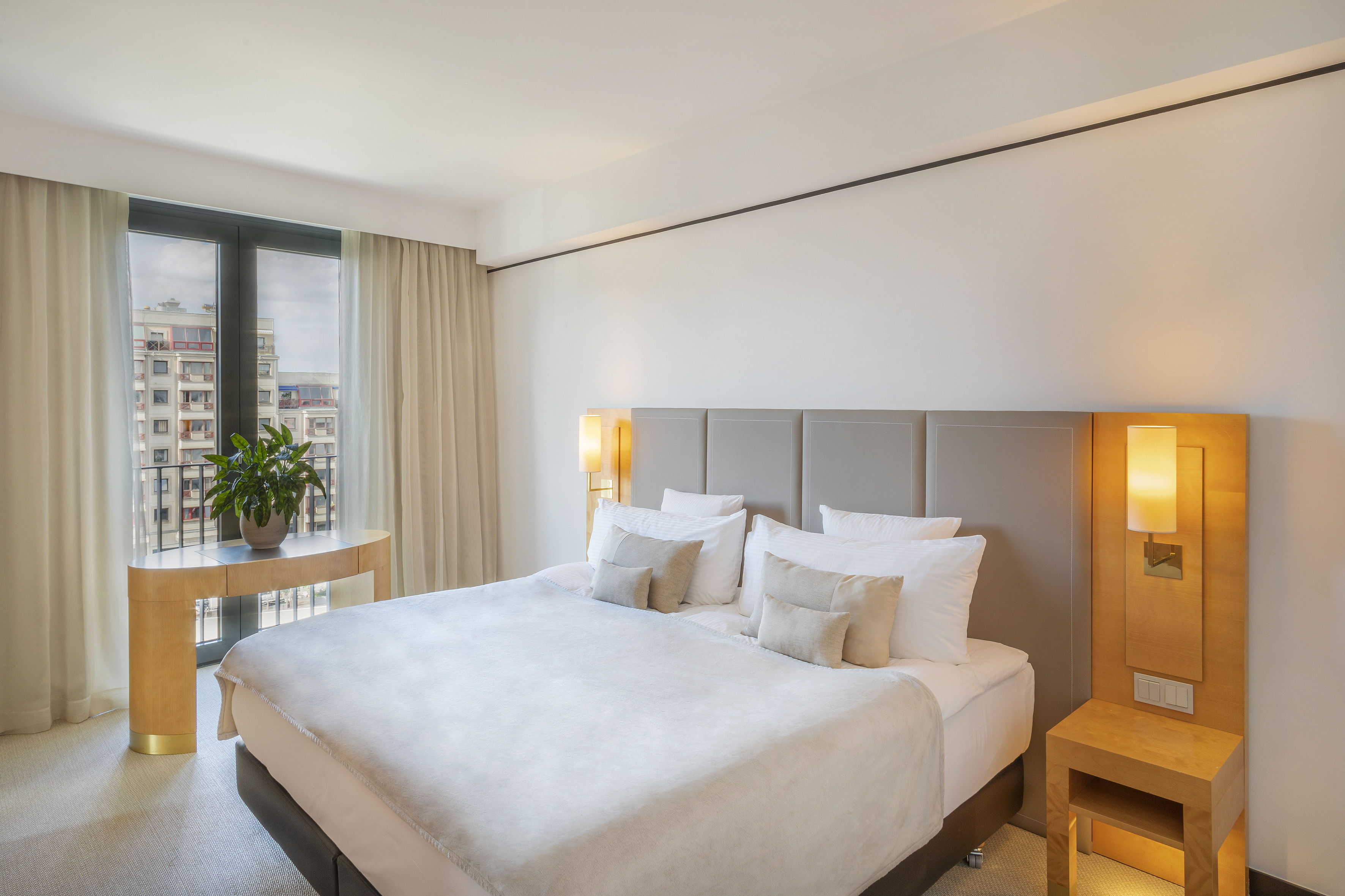 Modern hotel room with large bed, city view from window, and sleek decor.