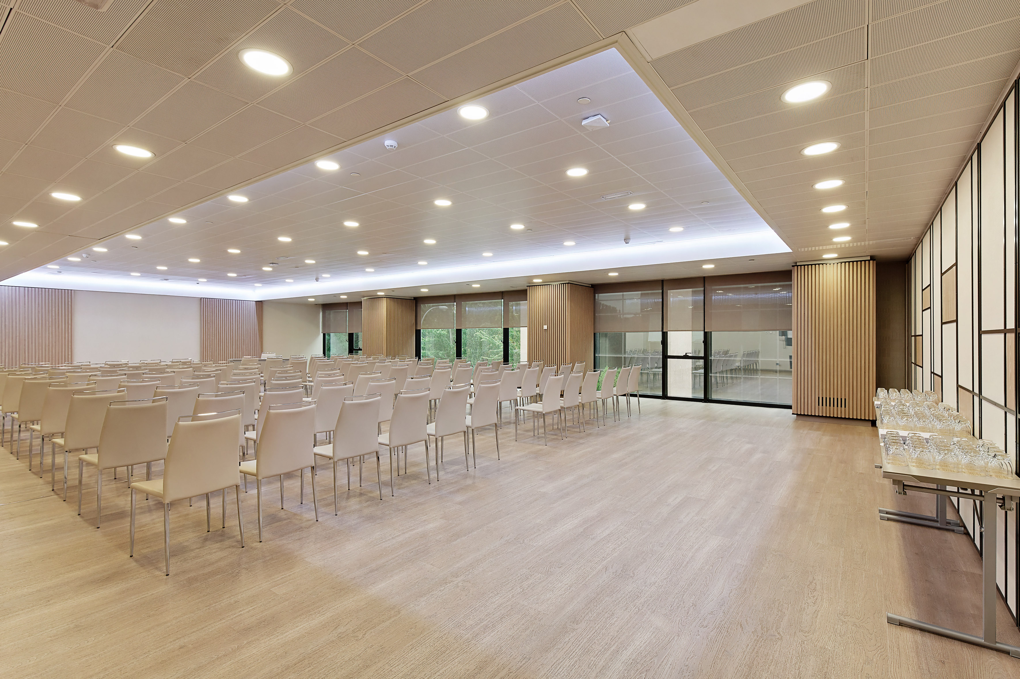 Modern conference room with rows of chairs, light wood floor, and large windows.