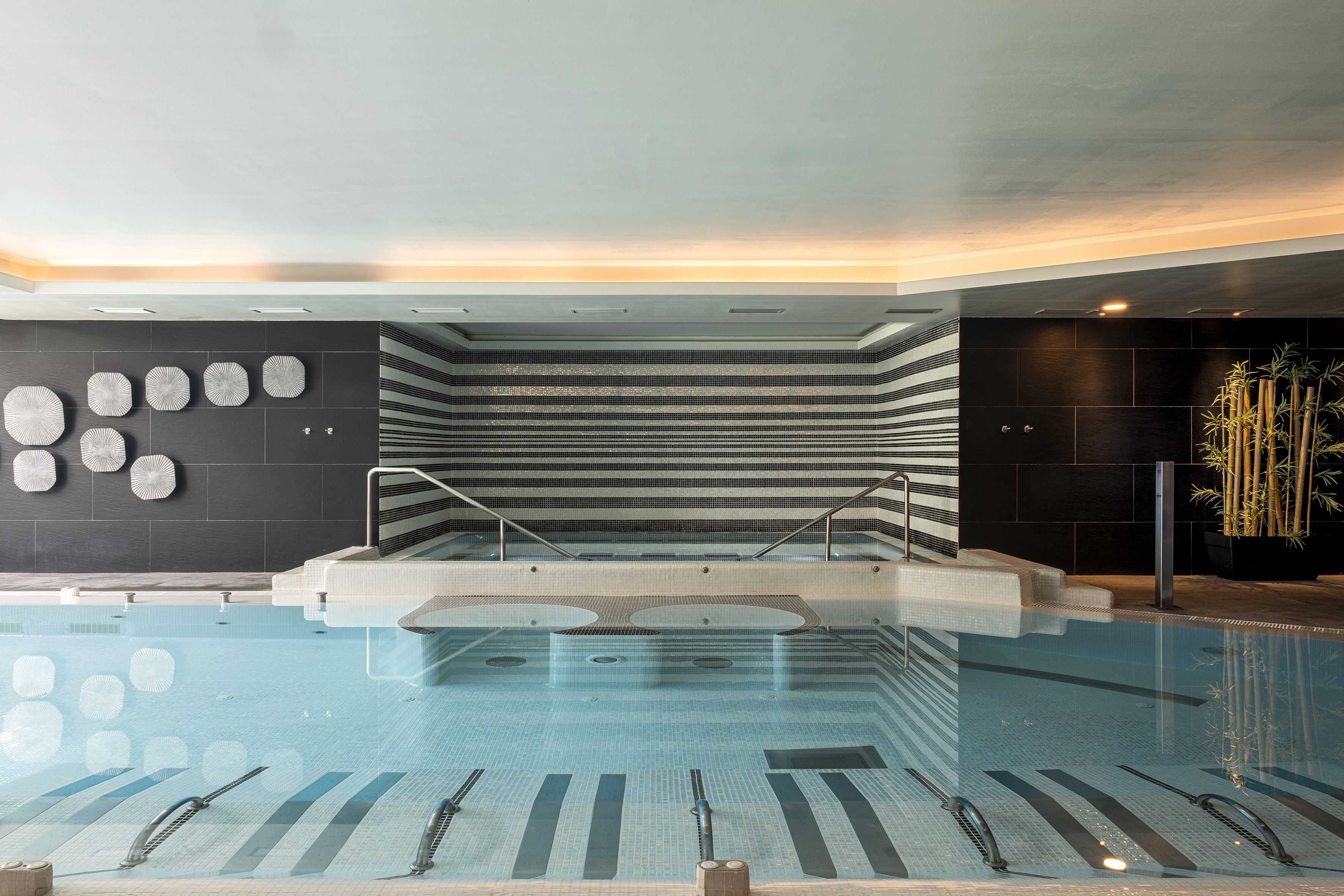Modern indoor pool with spa area, black and white striped tiles, and bamboo decor.