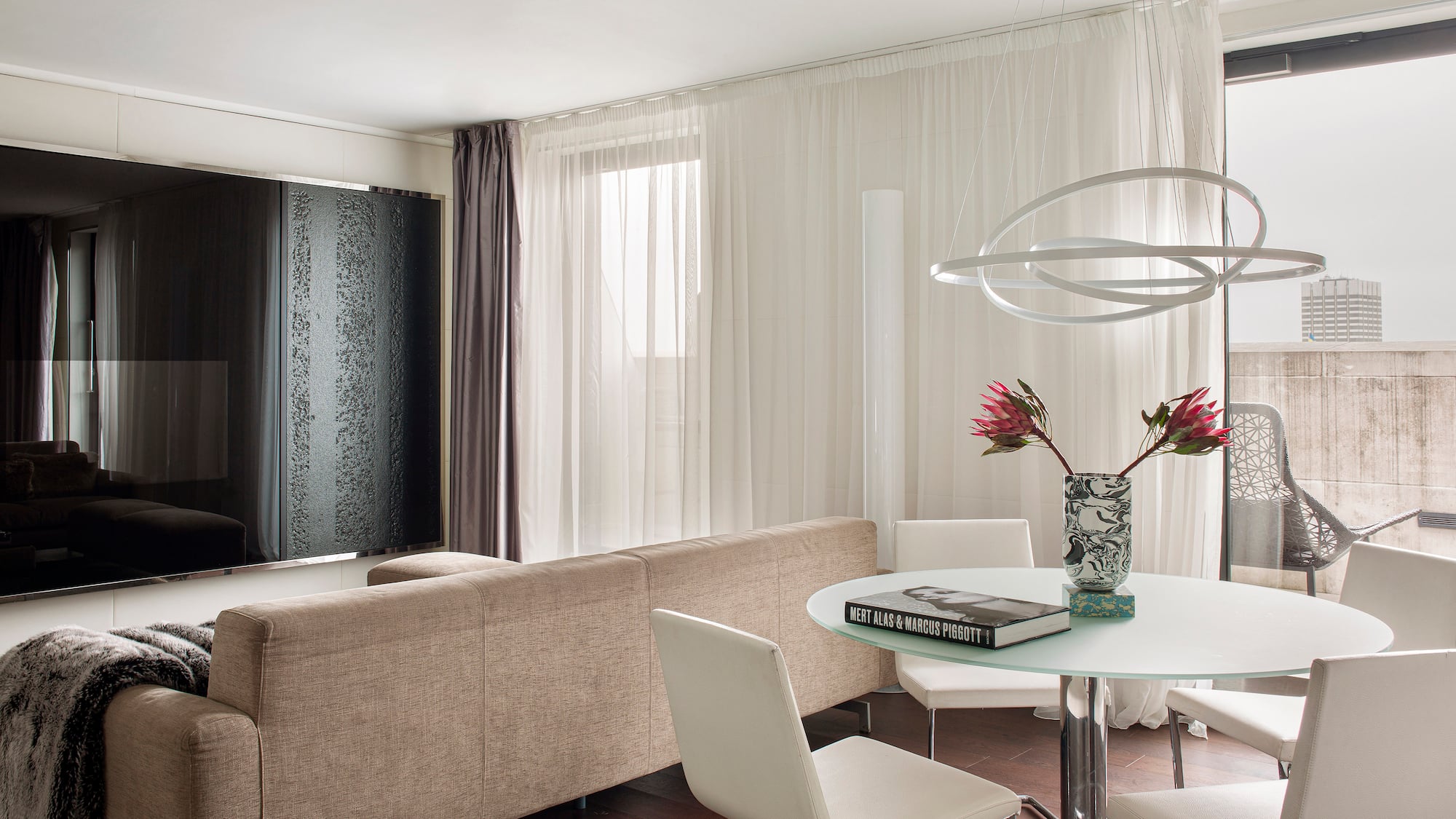 Modern living room with beige sofa, glass dining table, and unique orb chandelier.
