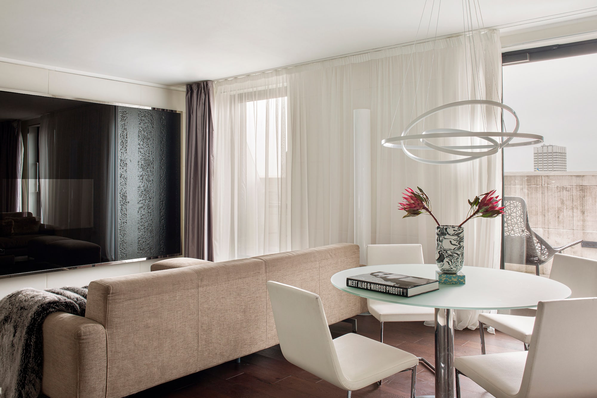 Modern living room with beige sofa, glass dining table, and unique orb chandelier.