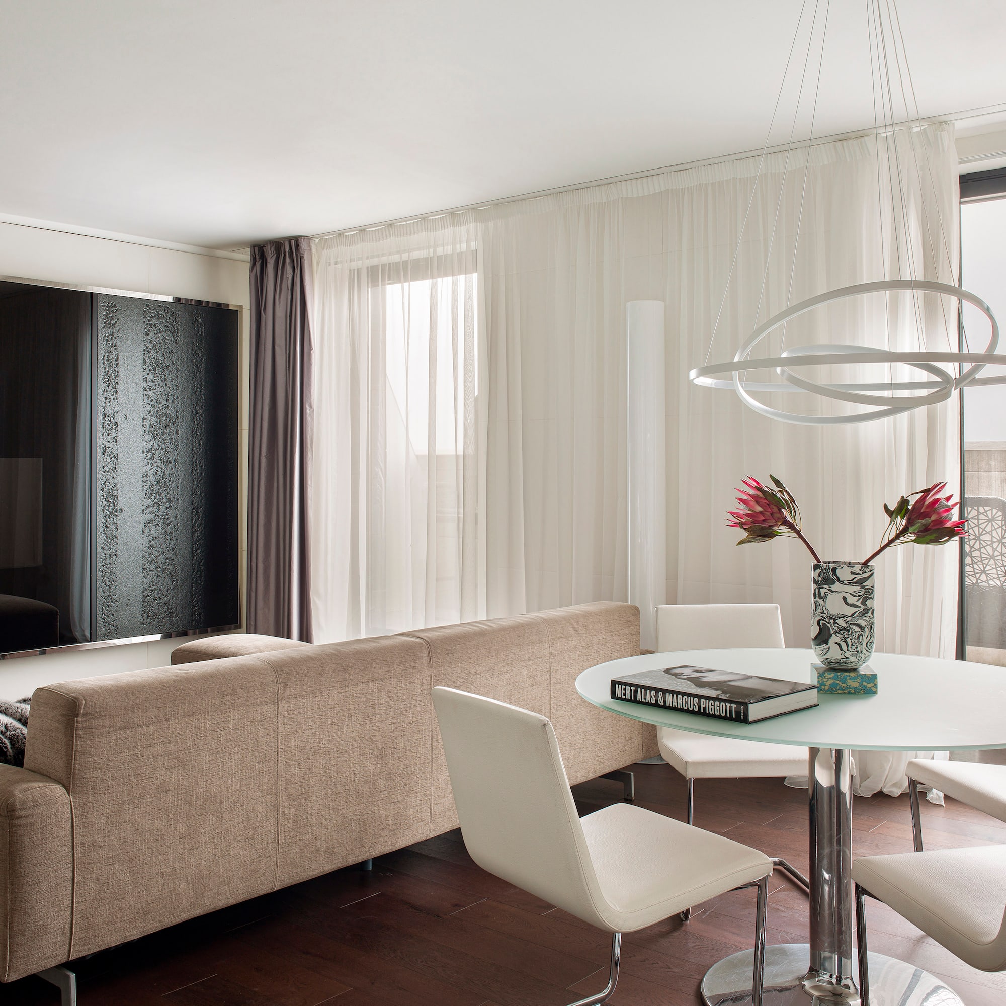 Modern living room with beige sofa, glass dining table, and unique orb chandelier.