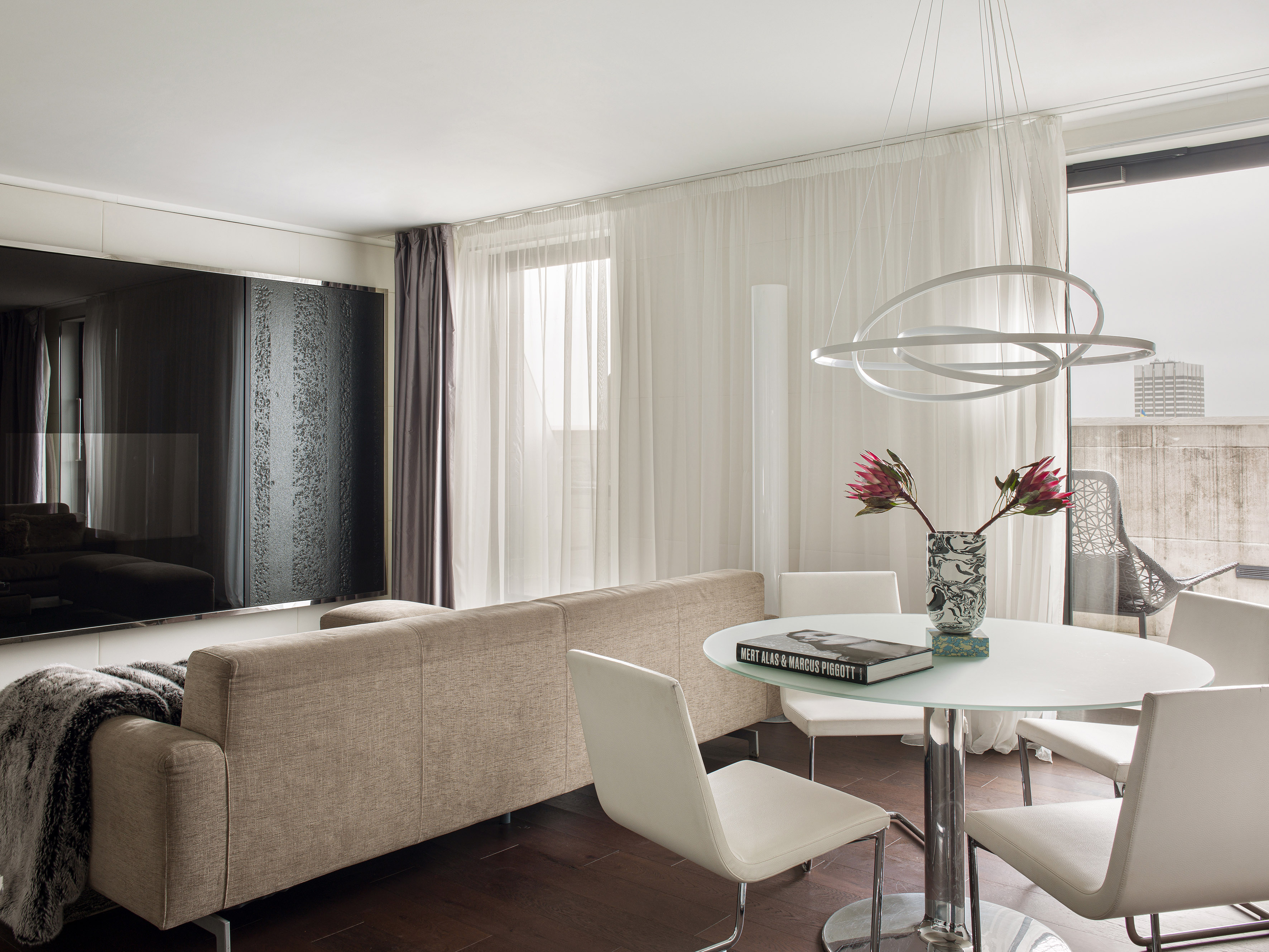 Modern living room with beige sofa, glass dining table, and unique orb chandelier.