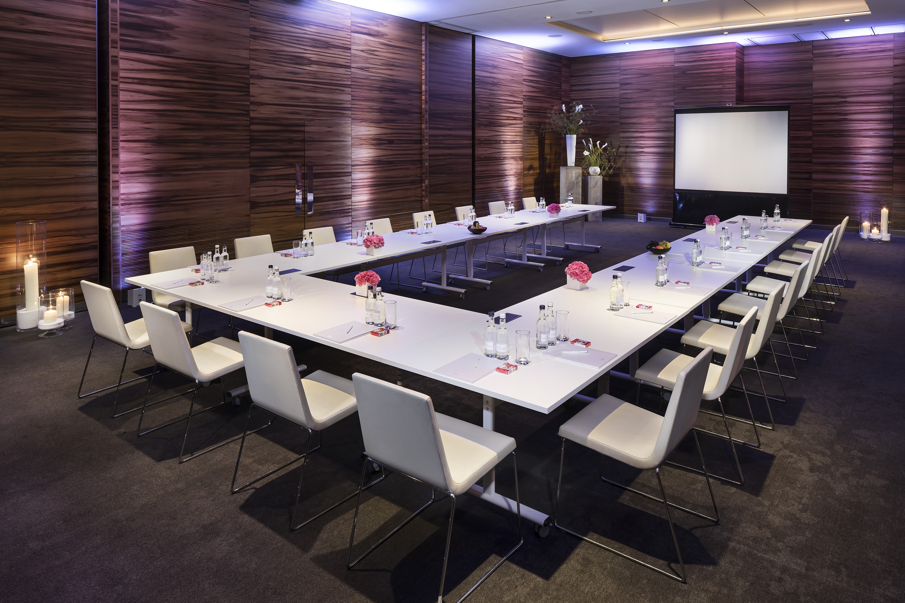 U-shaped meeting room with white tables, projector screen, and textured walls.
