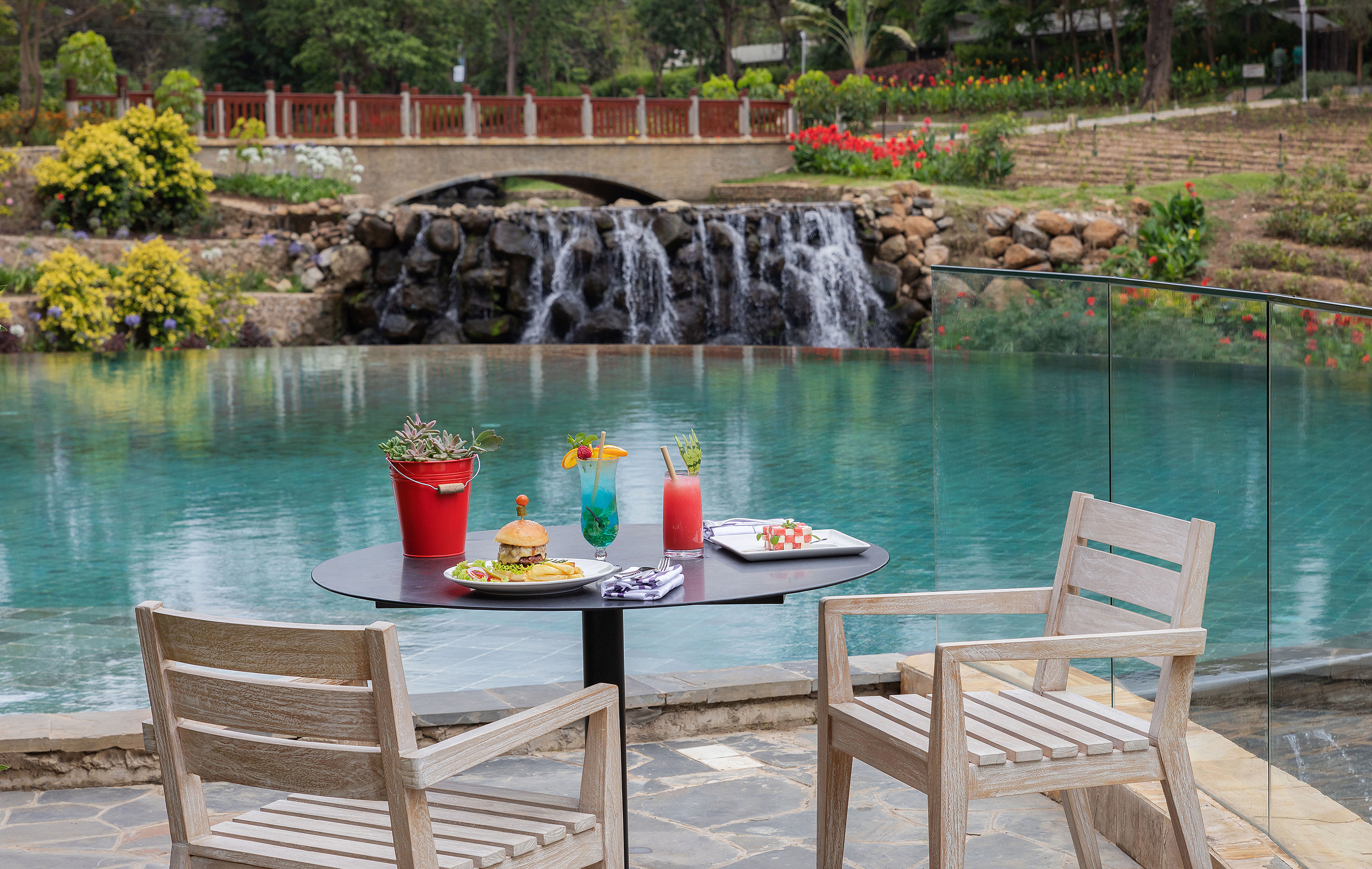 Poolside dining with burger, cocktails, waterfall, and garden bridge.