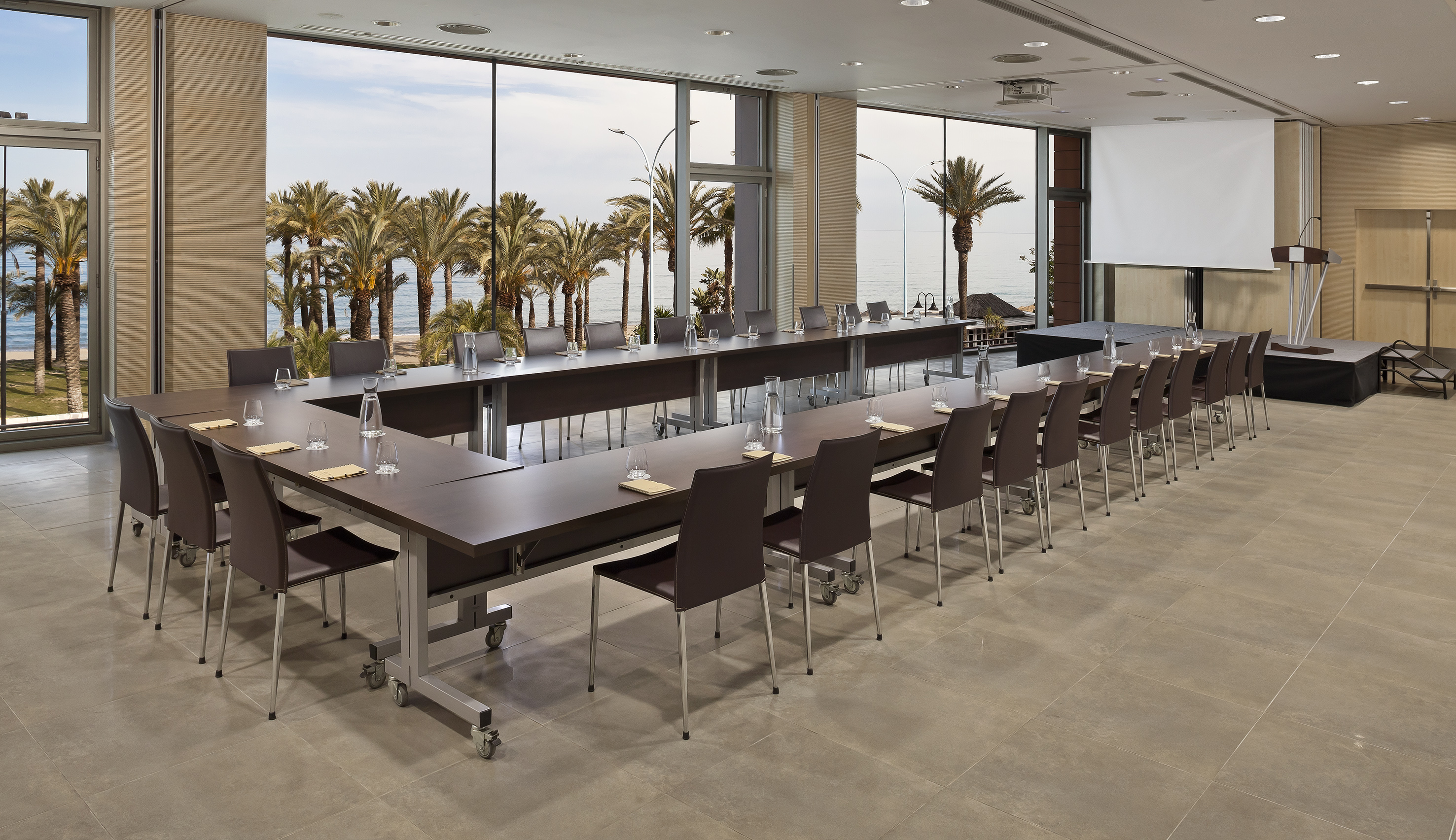 U-shaped conference room with beach view, palm trees, and projector screen.