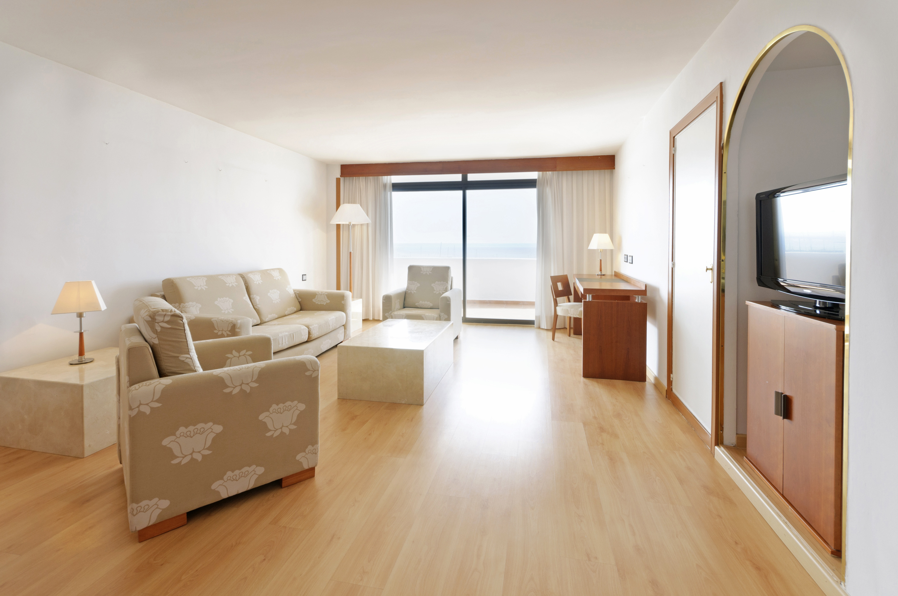 Spacious hotel living room with ocean view, balcony, and light wood flooring.