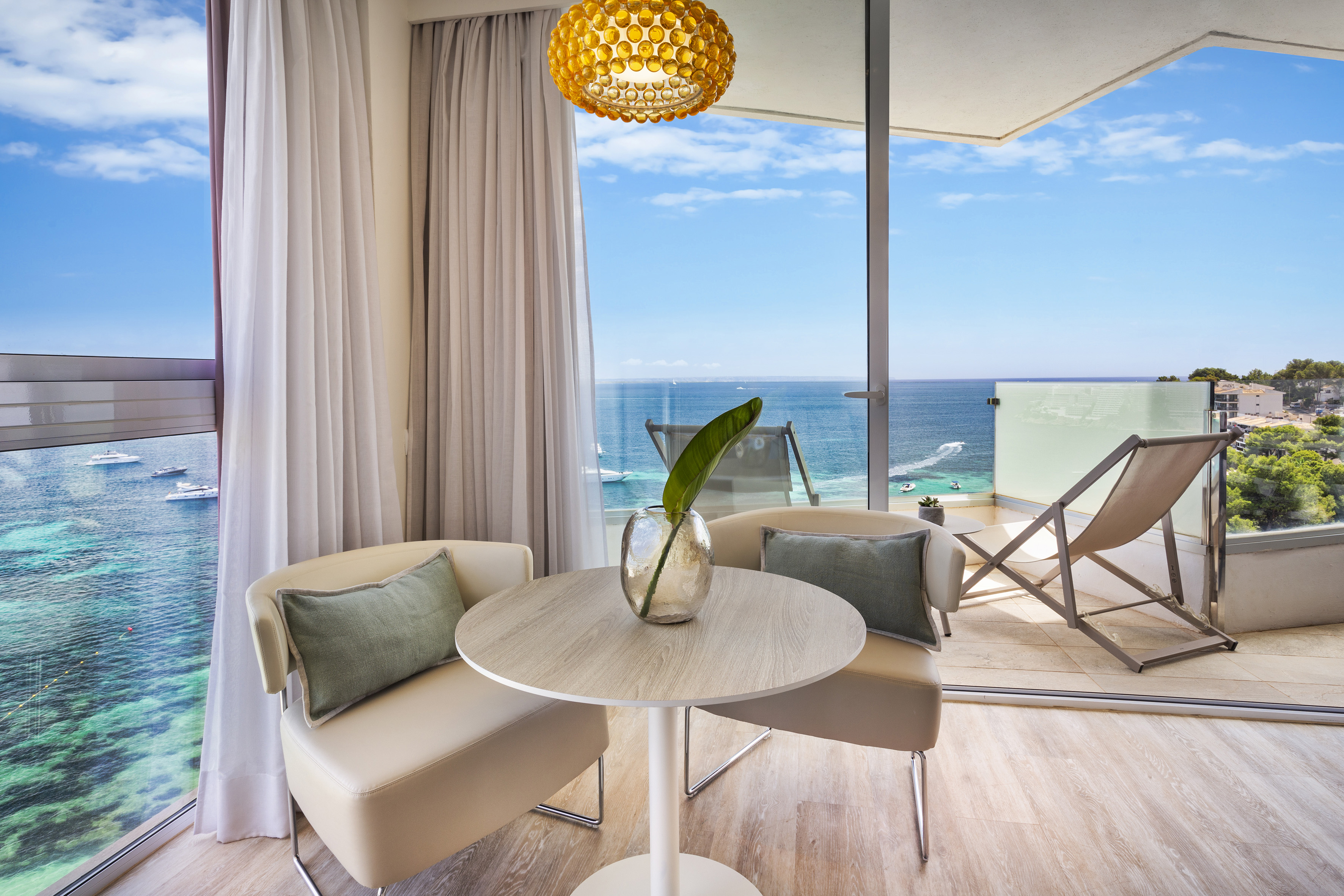Modern ocean view hotel room with balcony, seating, and clear blue sea.