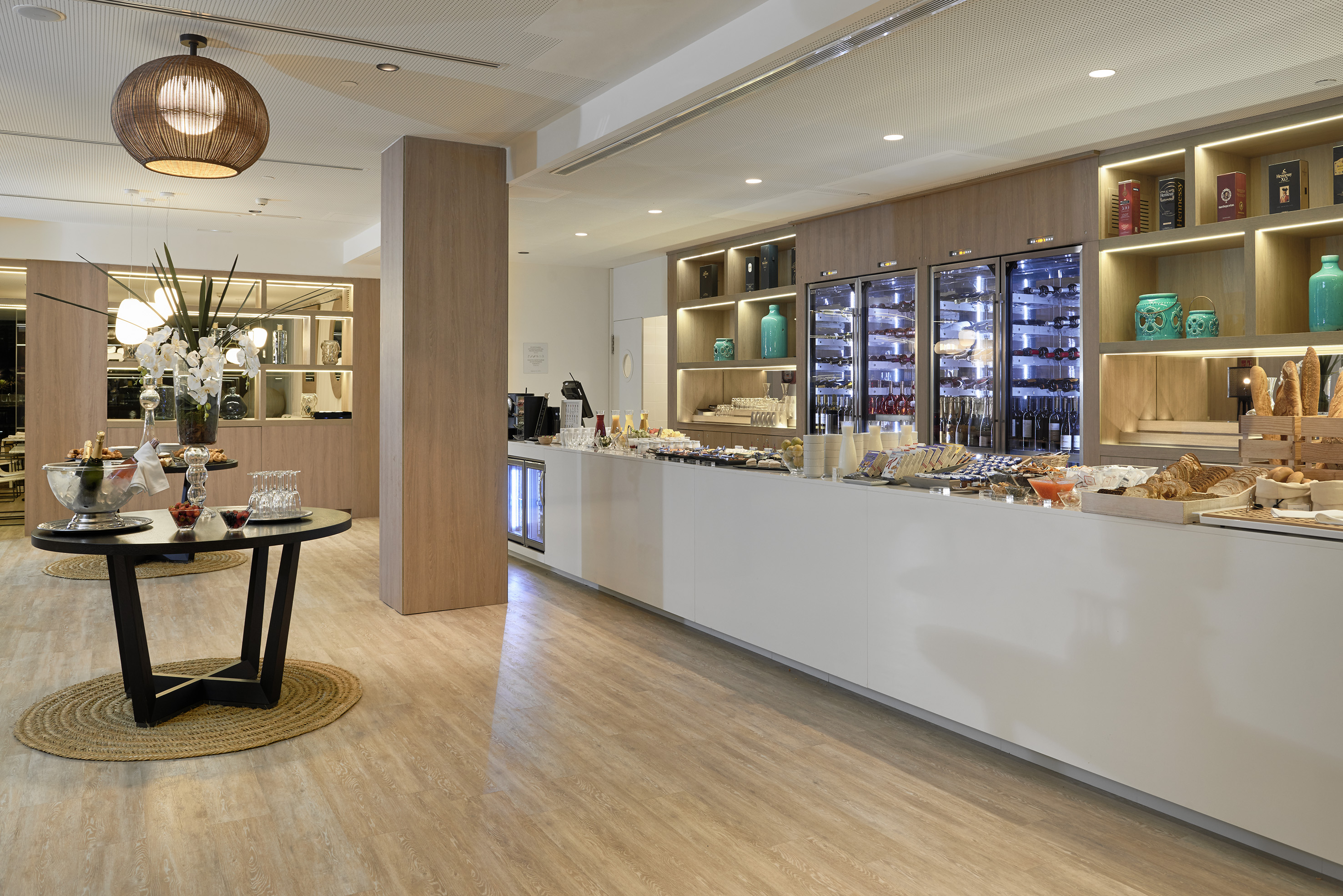 Modern hotel buffet lounge with food spread, wine coolers, and drinks.