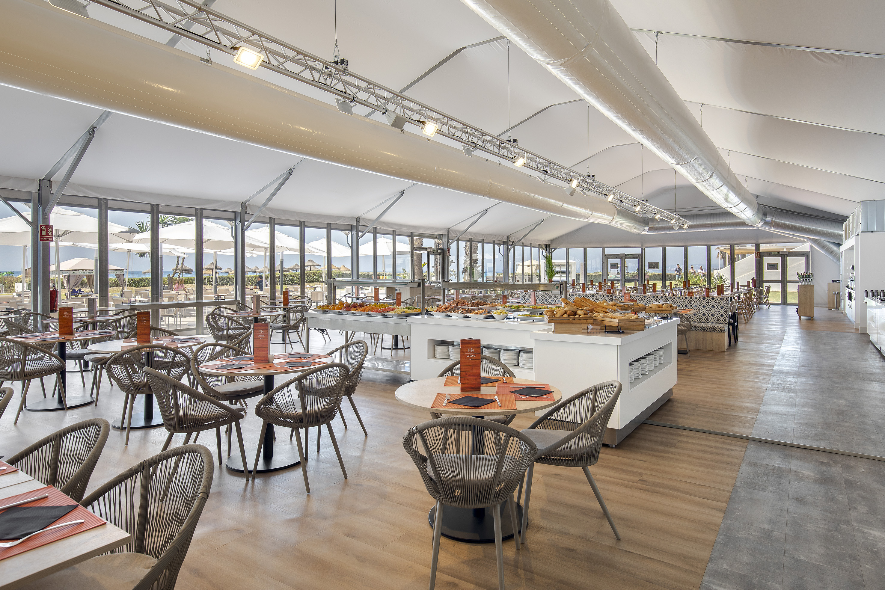 Bright resort buffet restaurant with food stations, dining tables, and ocean view.