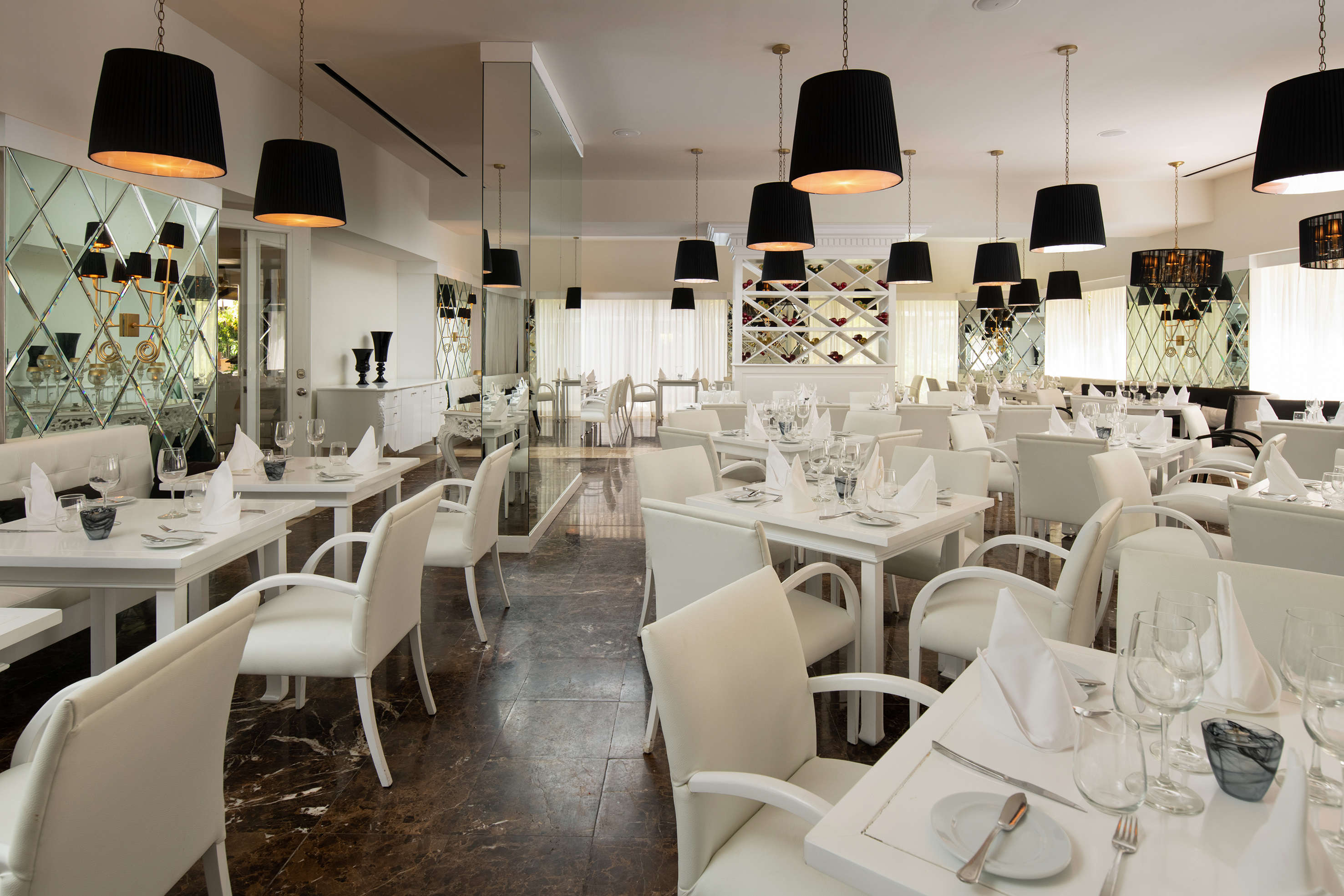 Elegant restaurant with white tables, chairs, black pendant lights, and dark marble floor.