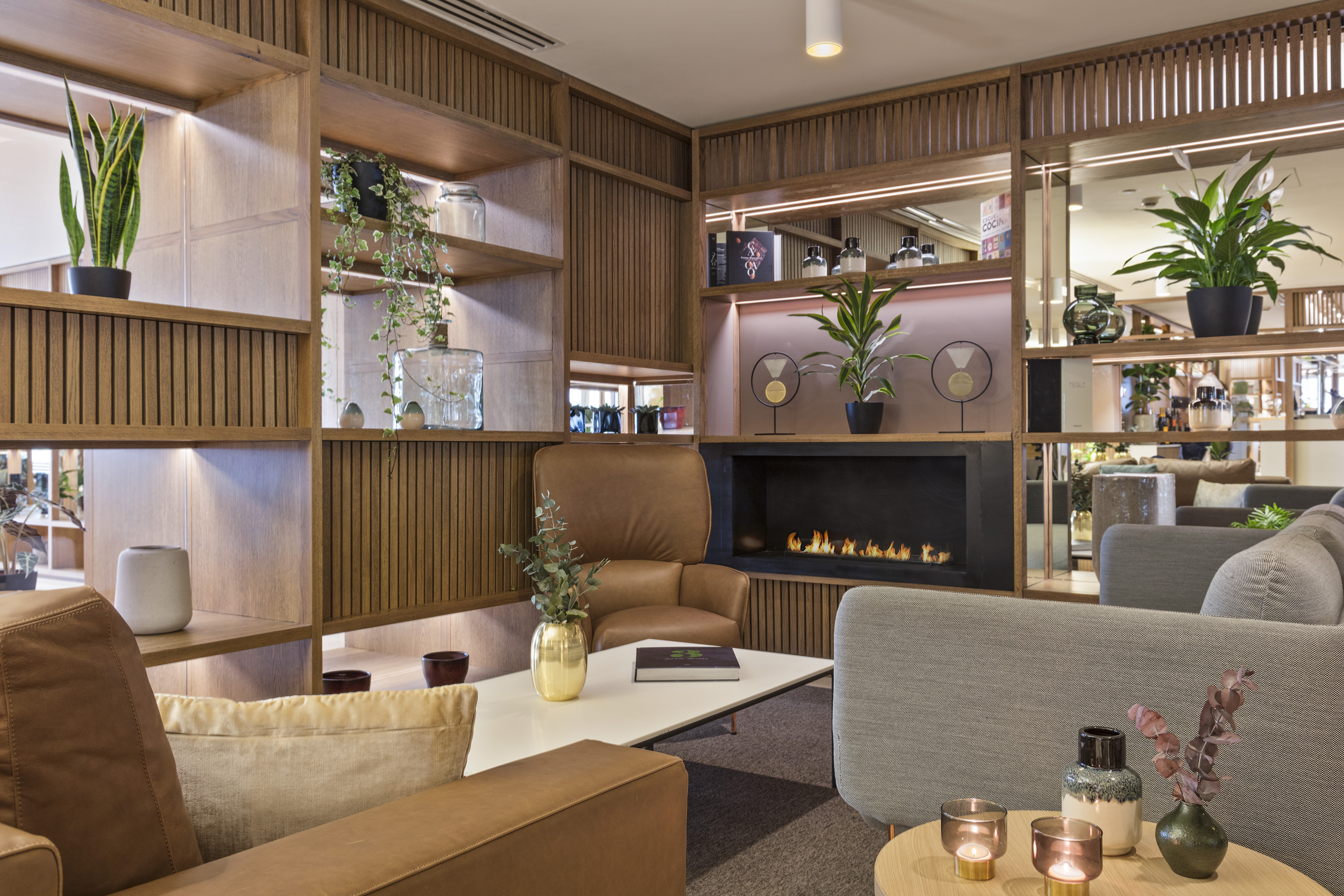 Modern lounge with a lit fireplace, wooden shelves, and comfortable seating.