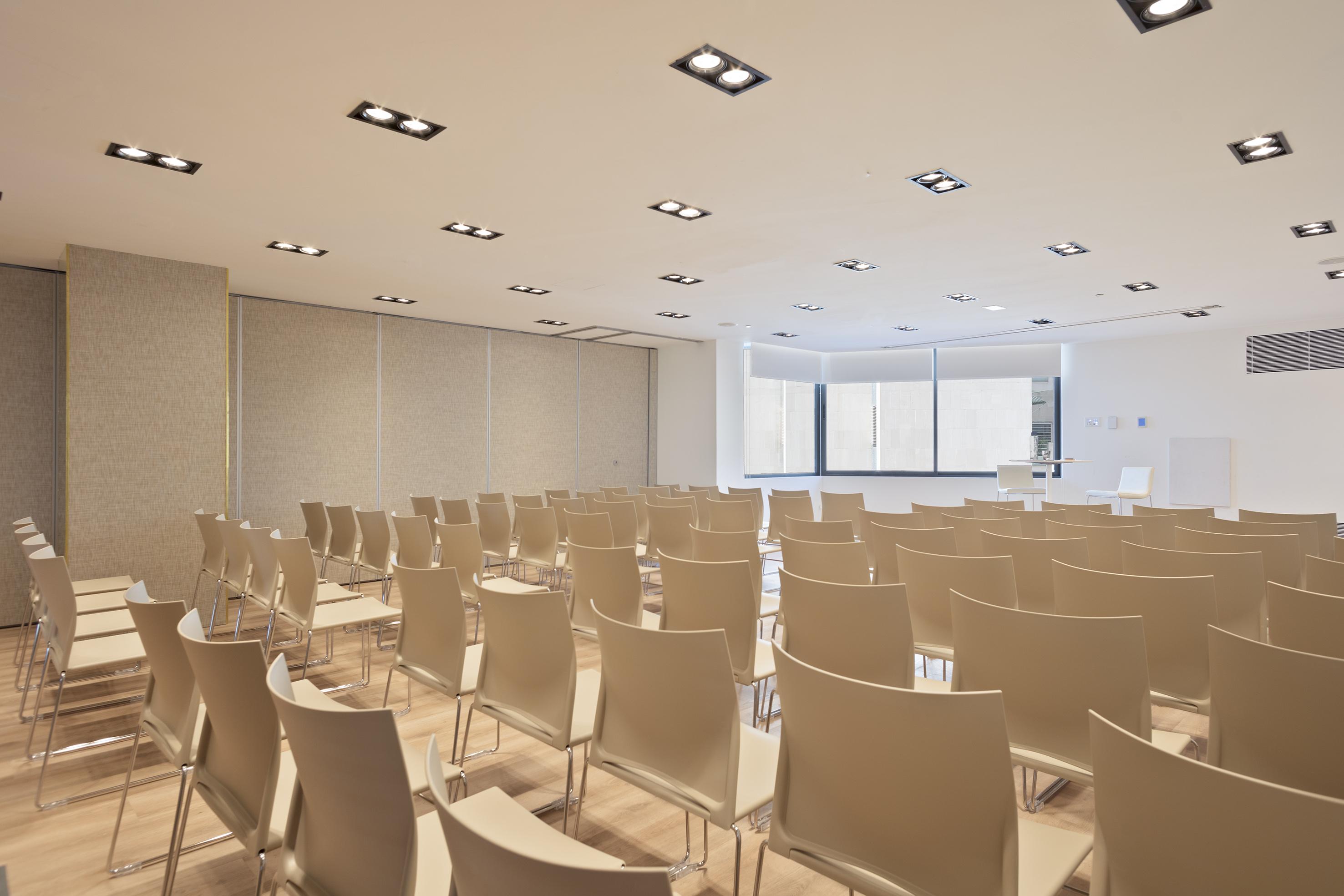 Empty modern conference room with beige chairs, light wood floor, ceiling lights.