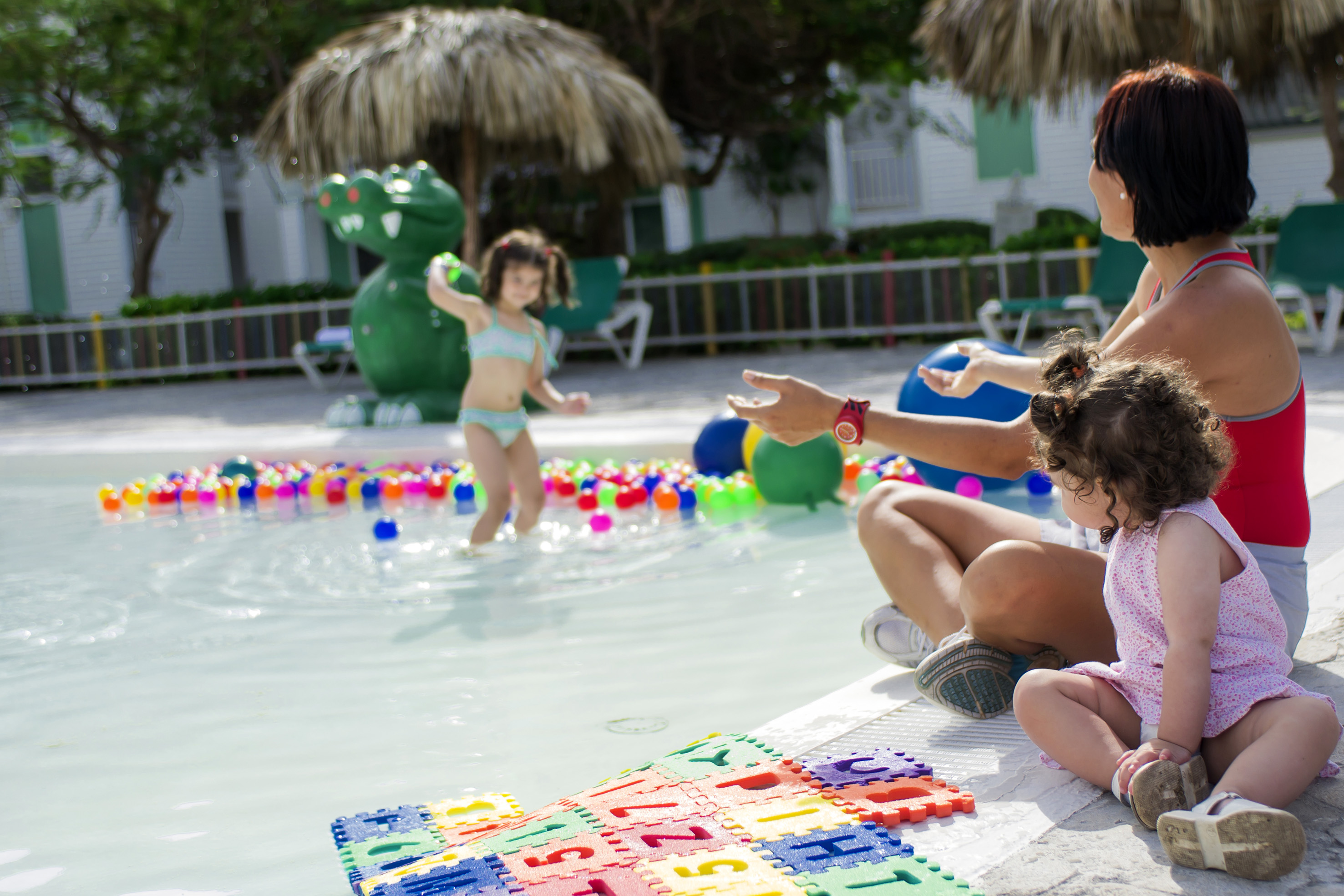 Kids and mom playing in a resort pool with colorful balls and alphabet mat.