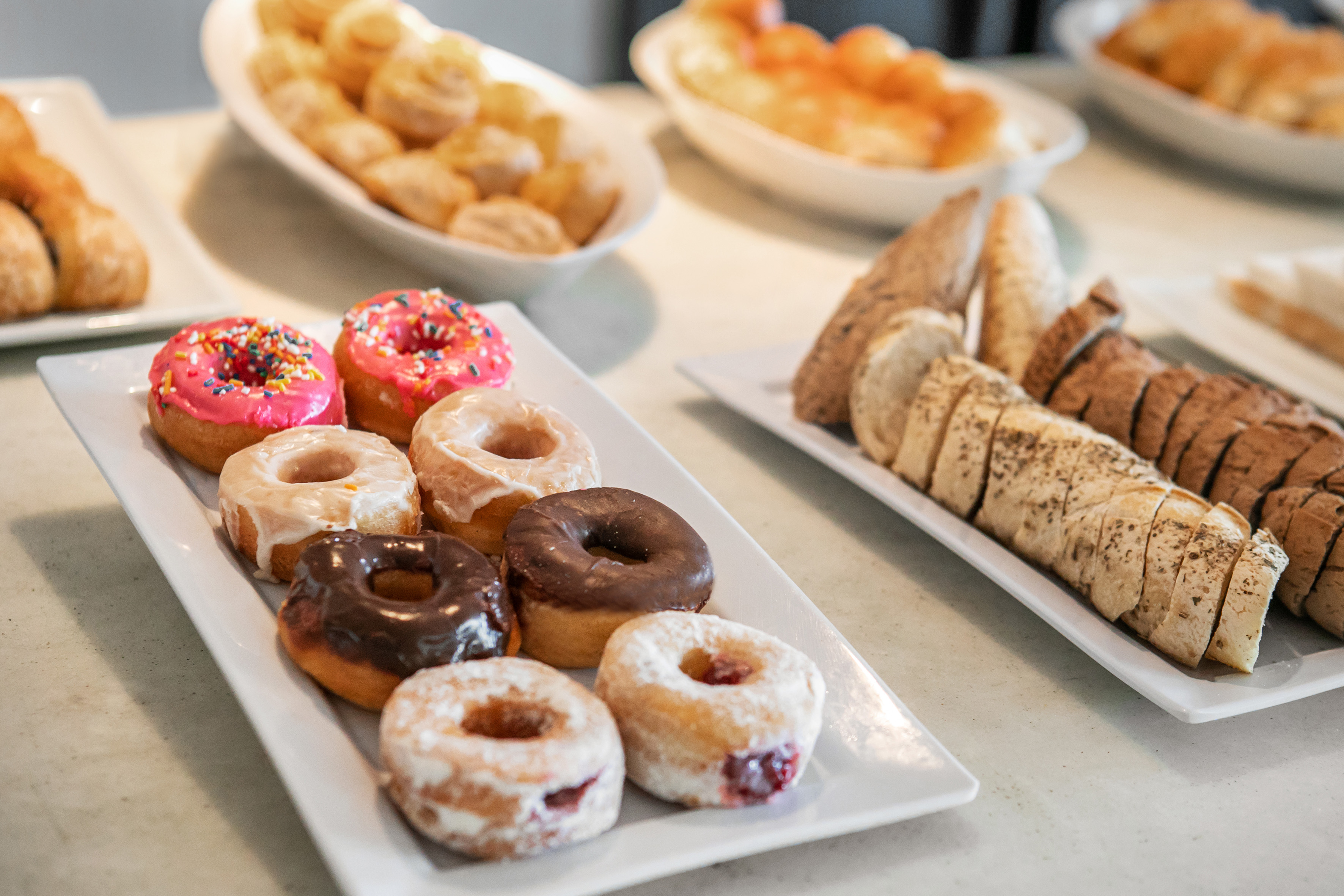 Assorted glazed, sprinkled, and jelly donuts with sliced bread and pastries on platters.