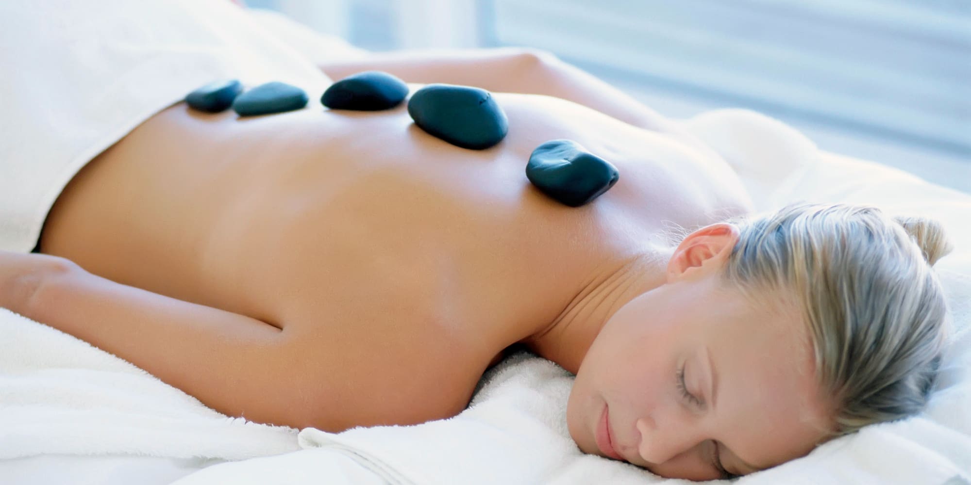 a woman lying on a white towel with black stones on her back