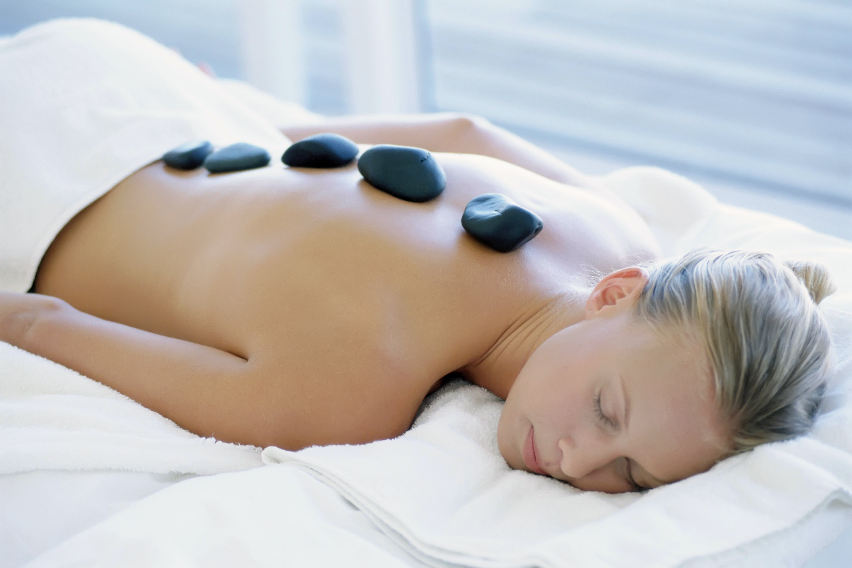 a woman lying on a white towel with black stones on her back