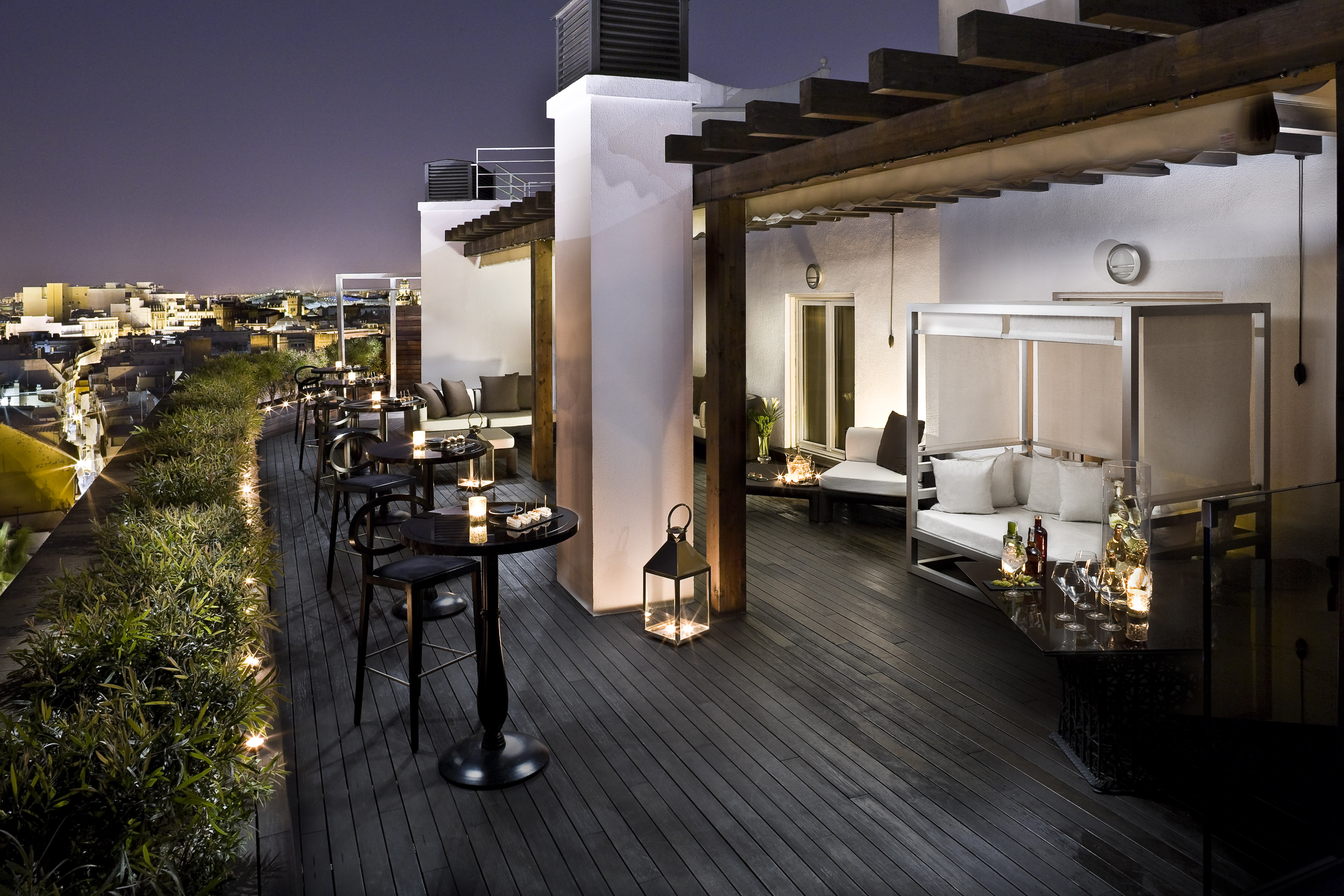 Rooftop terrace bar at night with city view, lounge seating, and ambient lights.