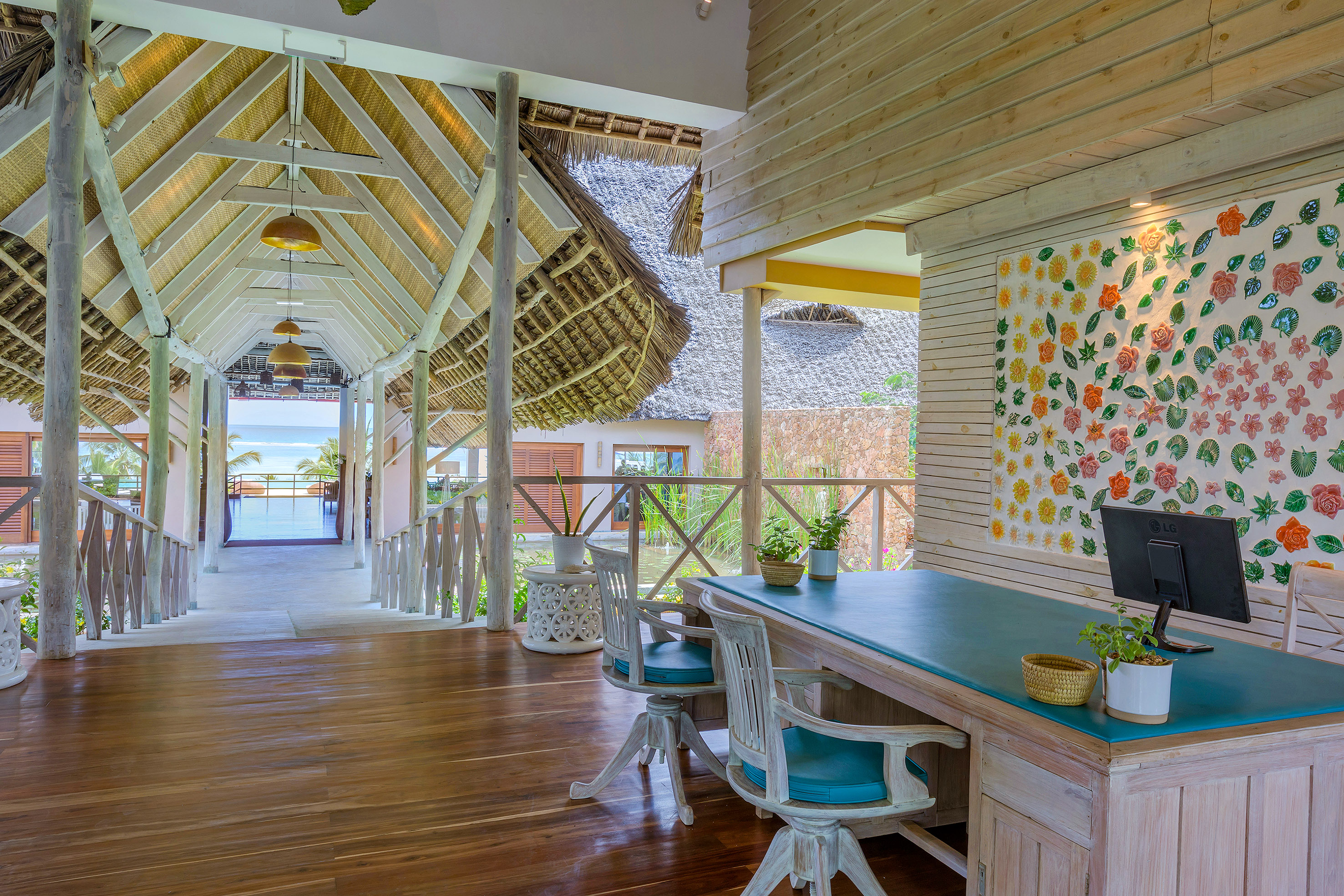 Tropical resort reception desk, ocean view, thatched roof, floral wall decor.
