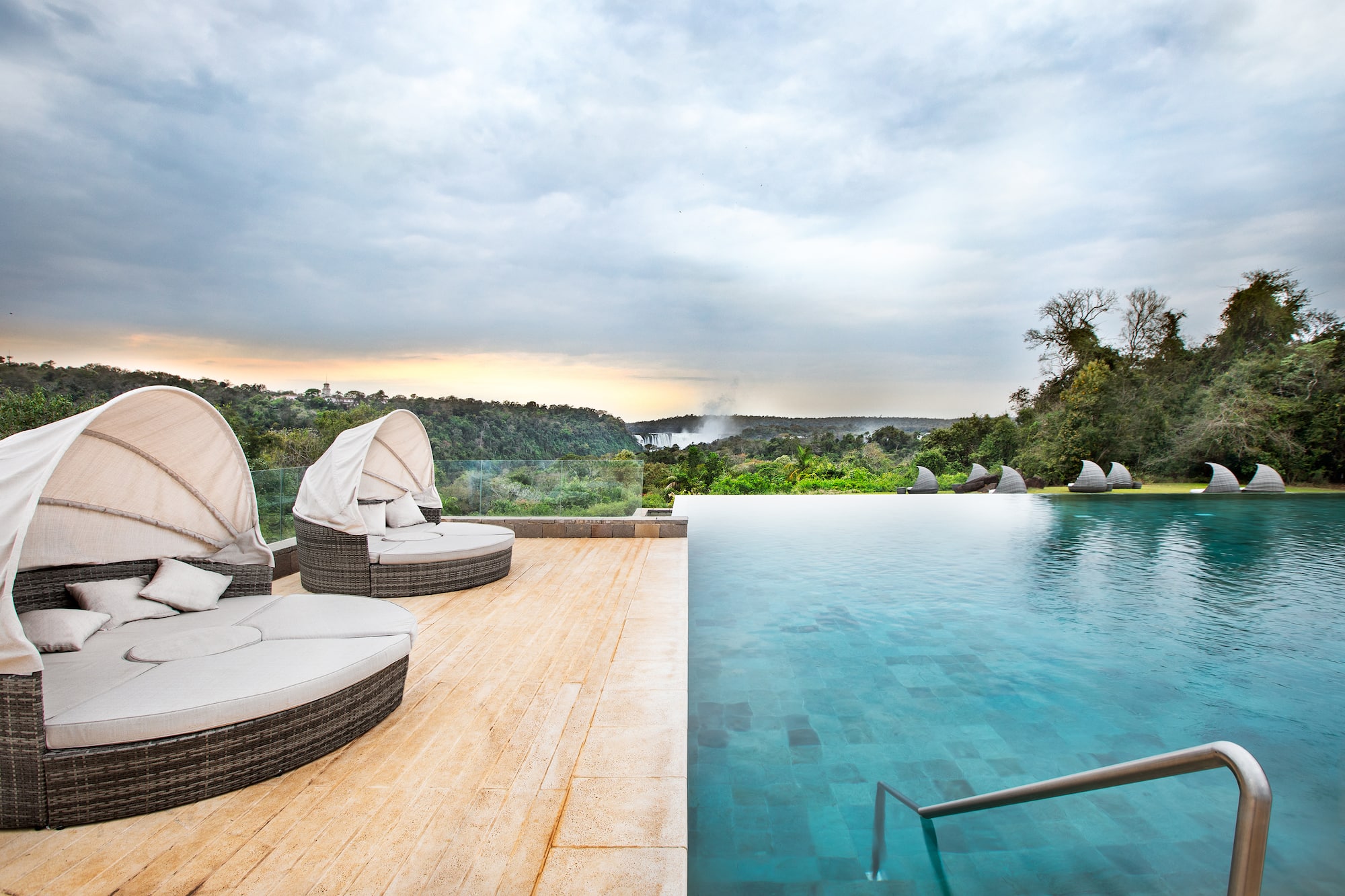 Luxury infinity pool with sun loungers overlooking Iguazu Falls and lush forest.